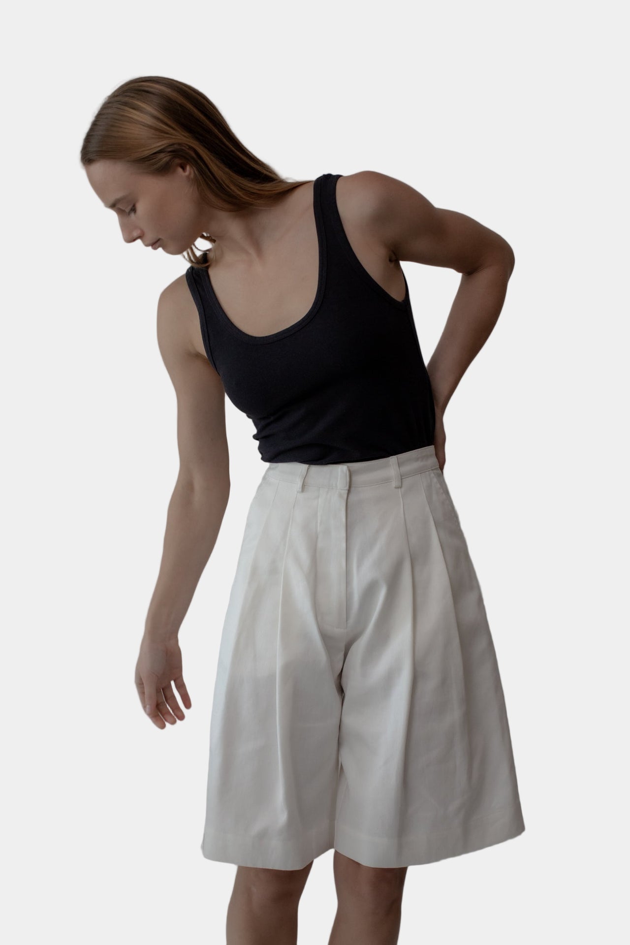 A person wearing a black tank top and white tailored shorts with a double front pleat and side entry pockets.