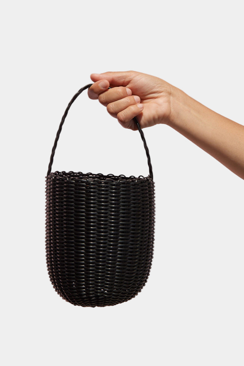 Hand holding a black woven basket against a pink background