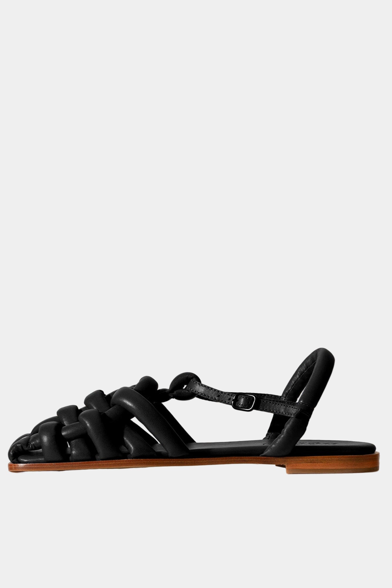 A black padded leather fisherman sandal with a square toe and flat sole, crafted in soft lambskin, with a buckle strap and displayed against a neutral background.