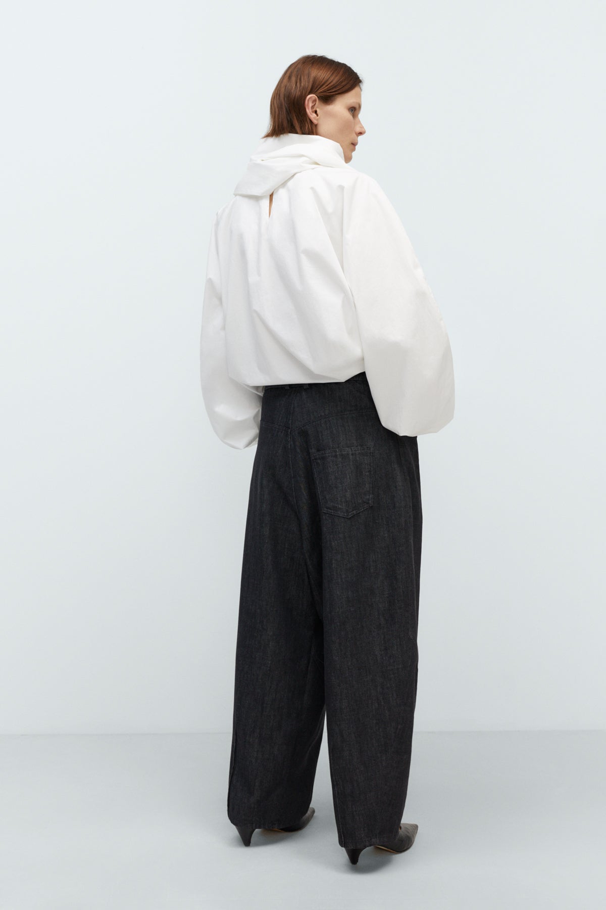 Person wearing a white oversized top and dark pants on a light gray background