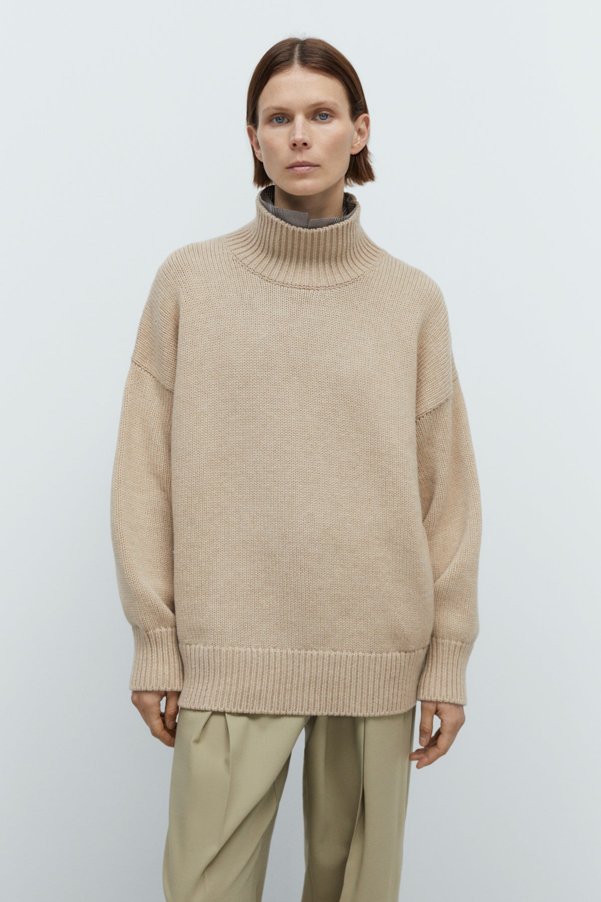 Person wearing a beige sweater and pants against a white background