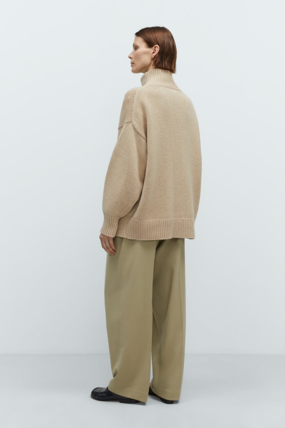 Person wearing a beige sweater and pants against a white background