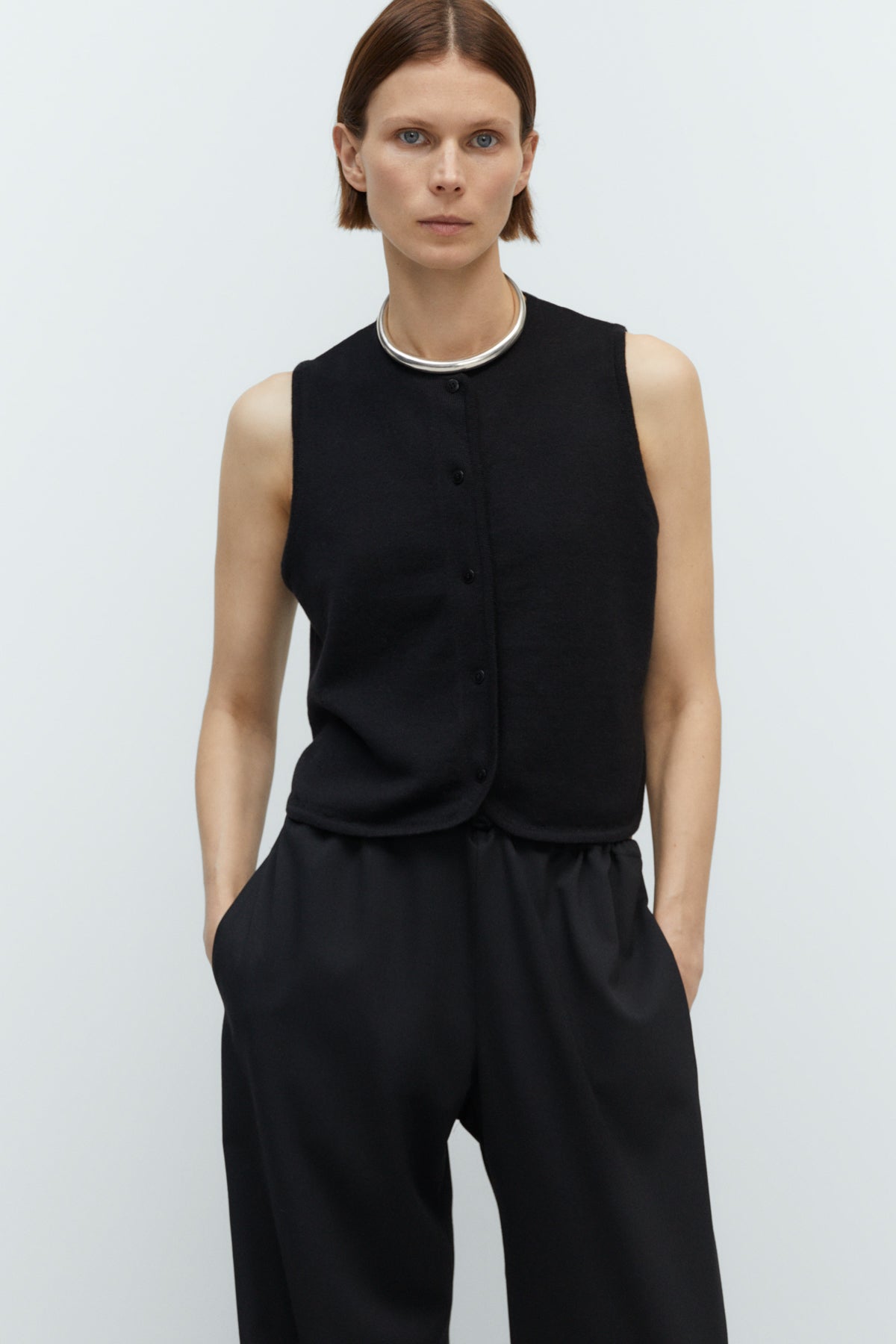 Person wearing a black sleeveless top and black pants on a white background