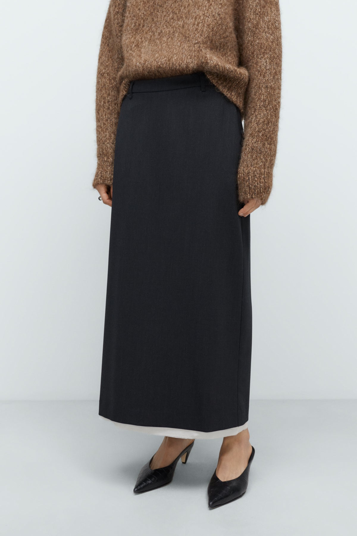 Woman wearing a brown sweater and black skirt on a white background