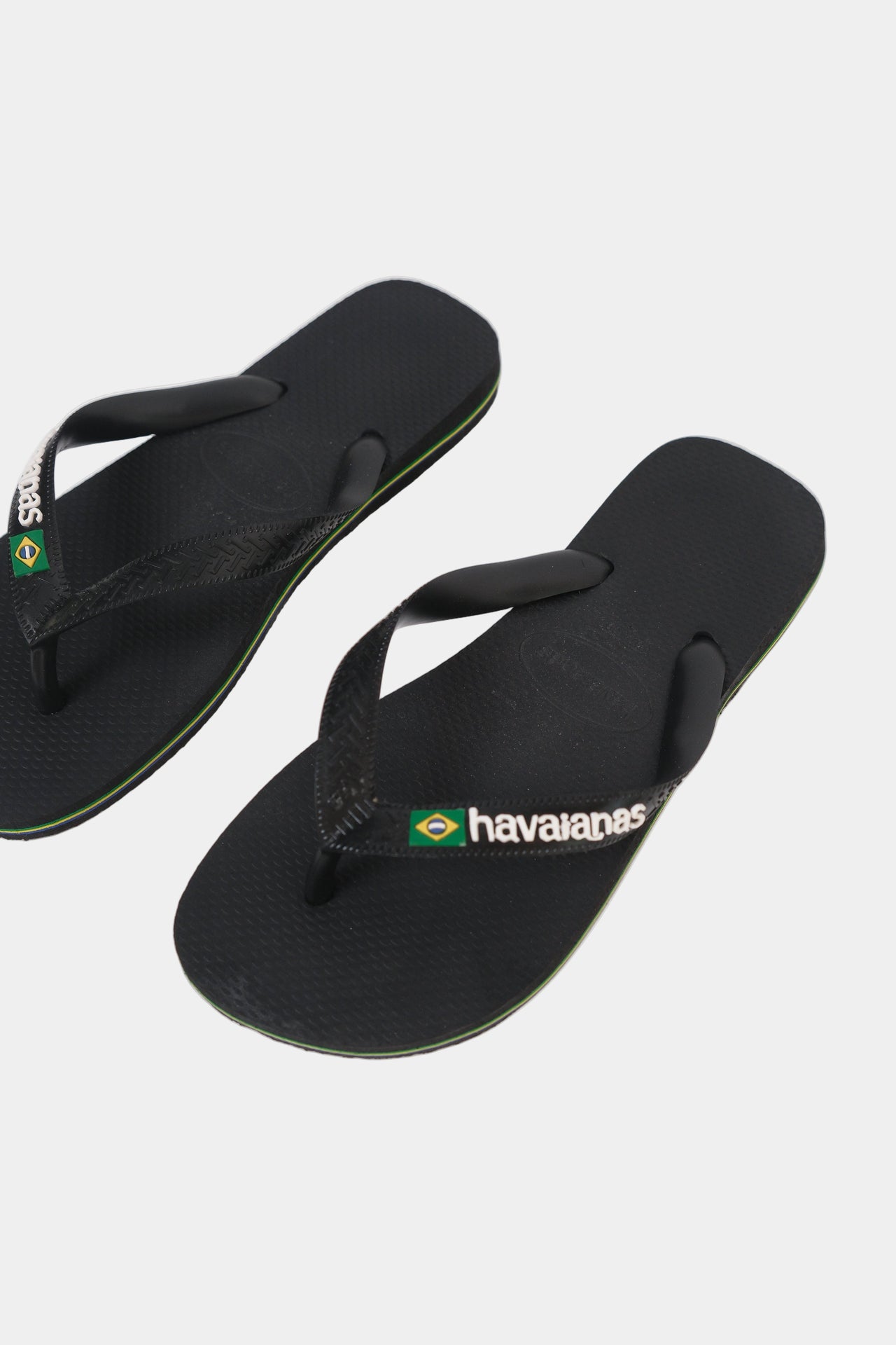A pair of black Havaianas flip-flops with a green and white Brazil flag and stripe design around the sole.