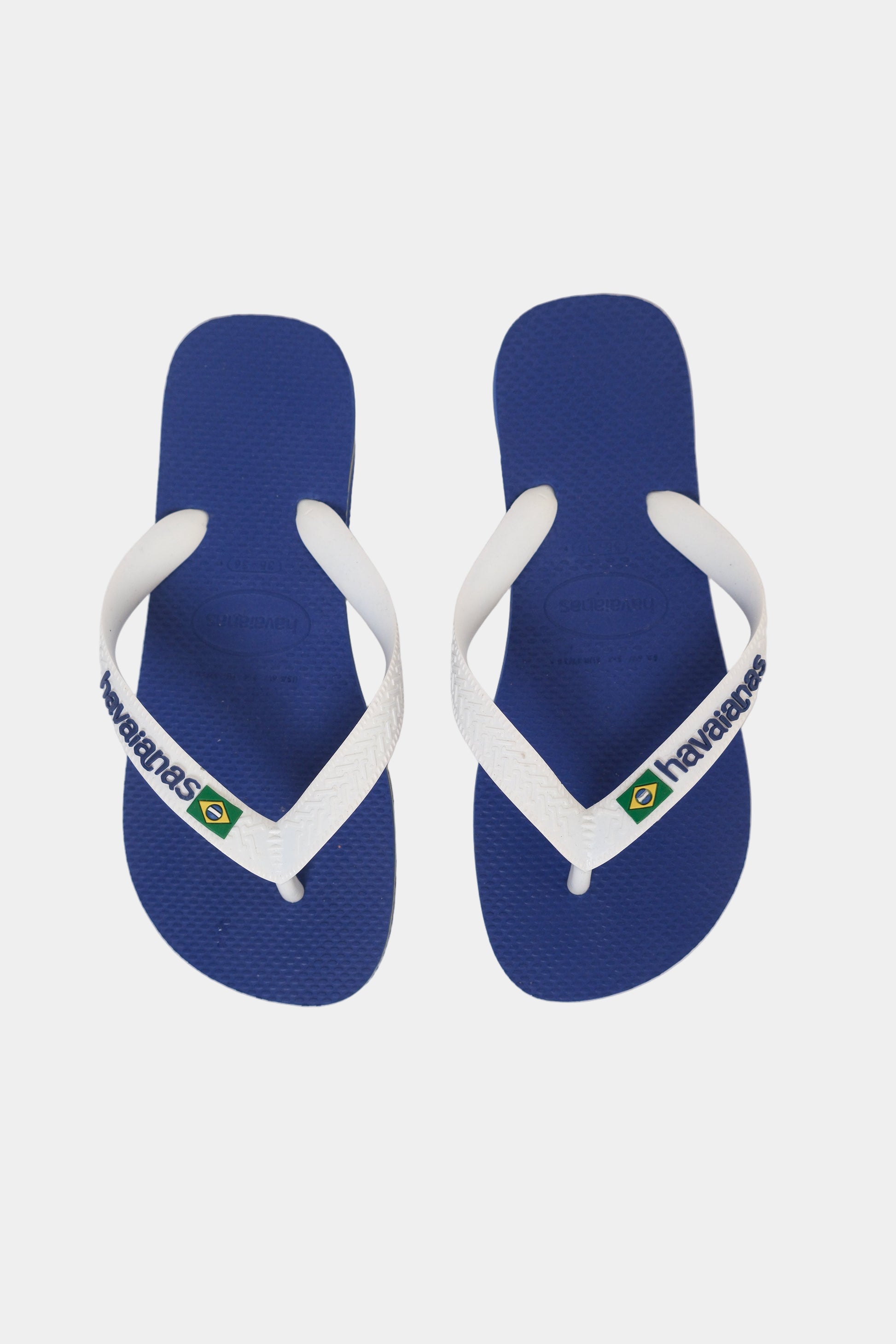 Pair of blue havaianas flip-flops with white straps on a light gray background