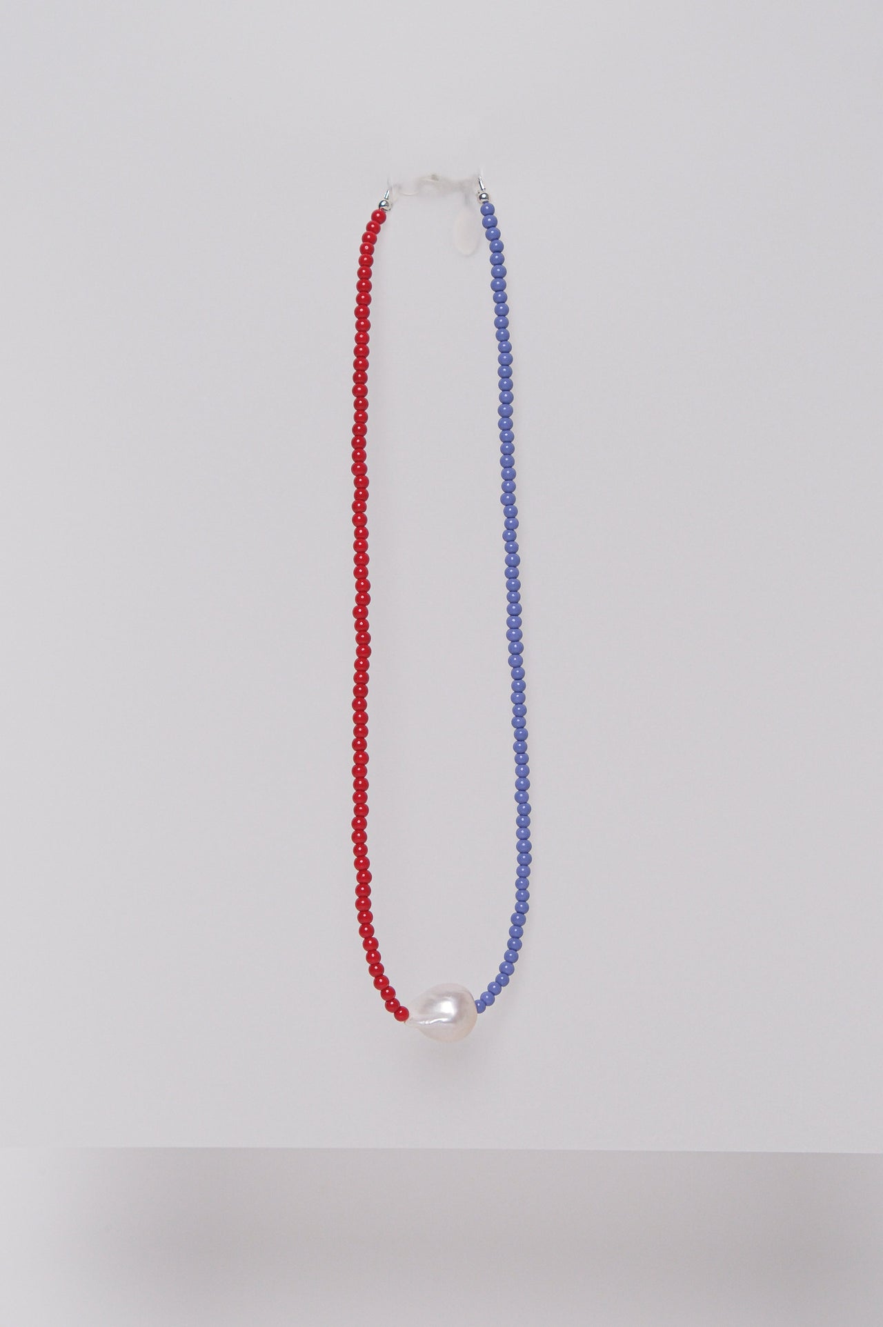 A two-tone beaded necklace with red and purple beads and a single pearl, displayed against a white background.