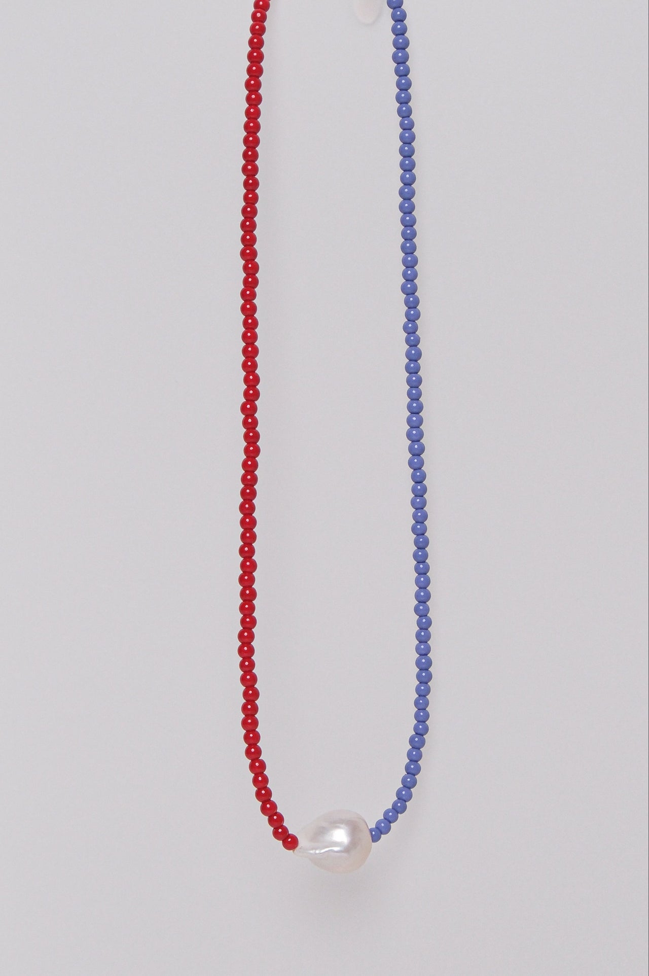 A two-tone beaded necklace with red and purple beads and a single pearl, displayed against a white background.