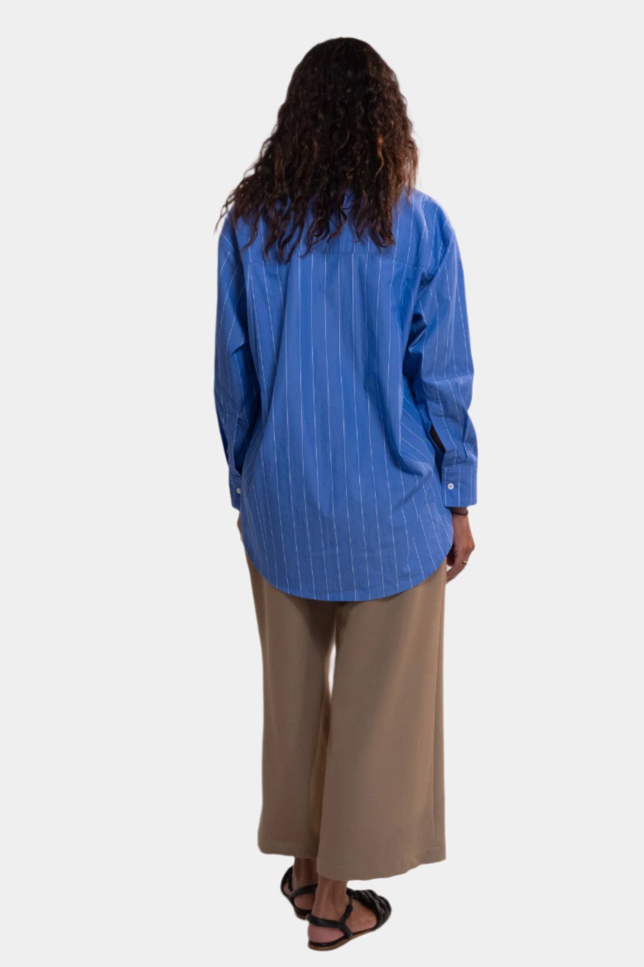 women wearing a cobalt blue stripe shirt and camel trousers against a plain background