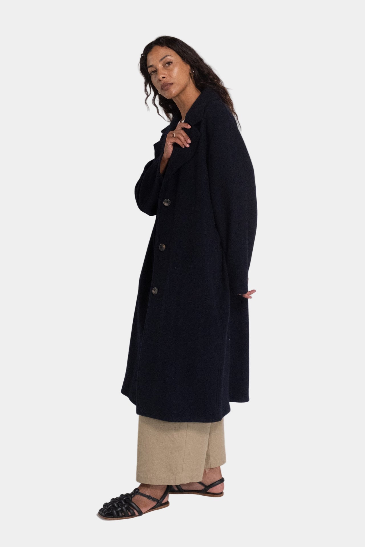 A woman modeling a navy longline tailored wool overcoat with notched lapels and a mid-calf length.