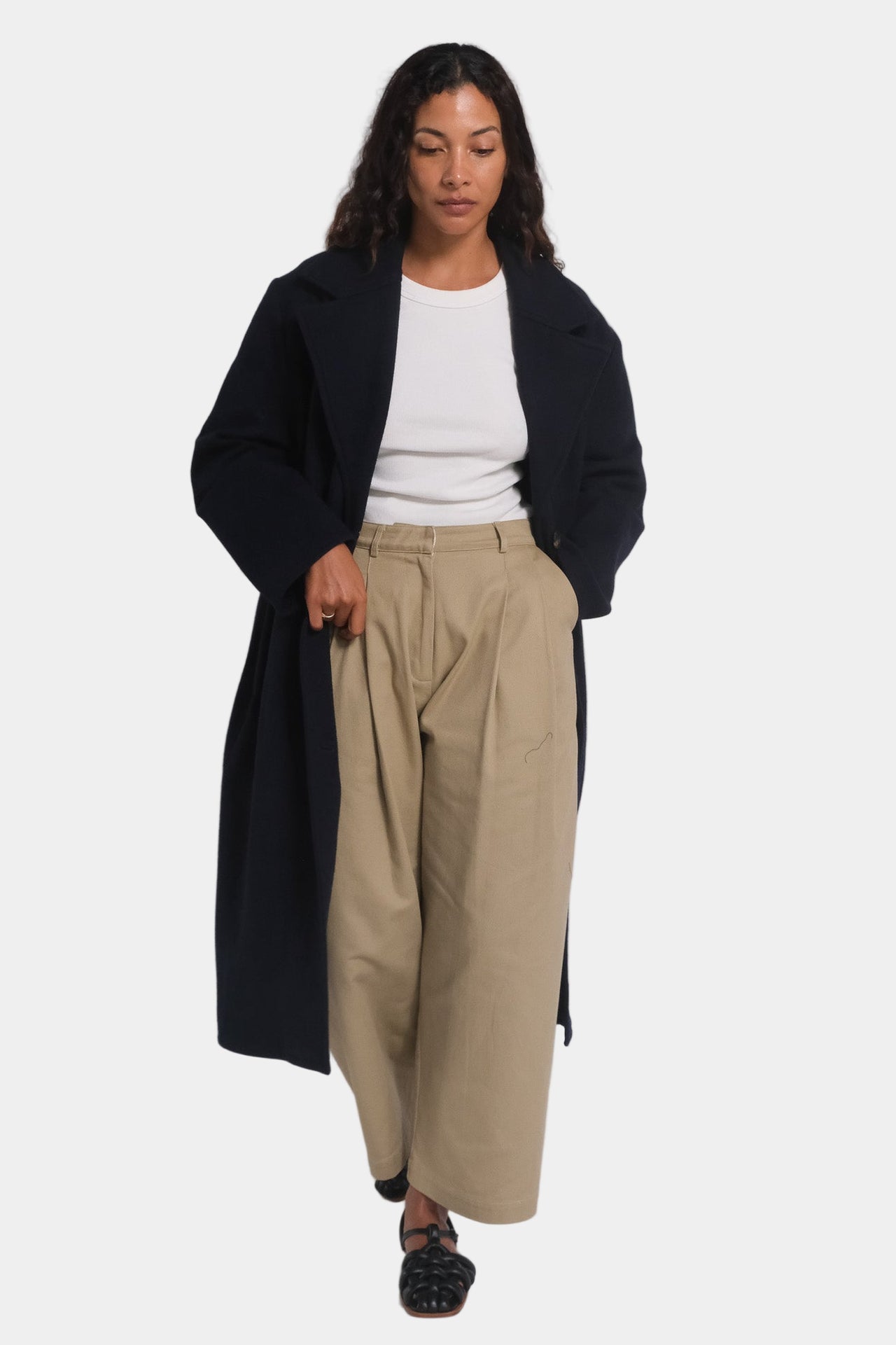 A woman modeling a navy longline tailored wool overcoat with notched lapels and a mid-calf length.