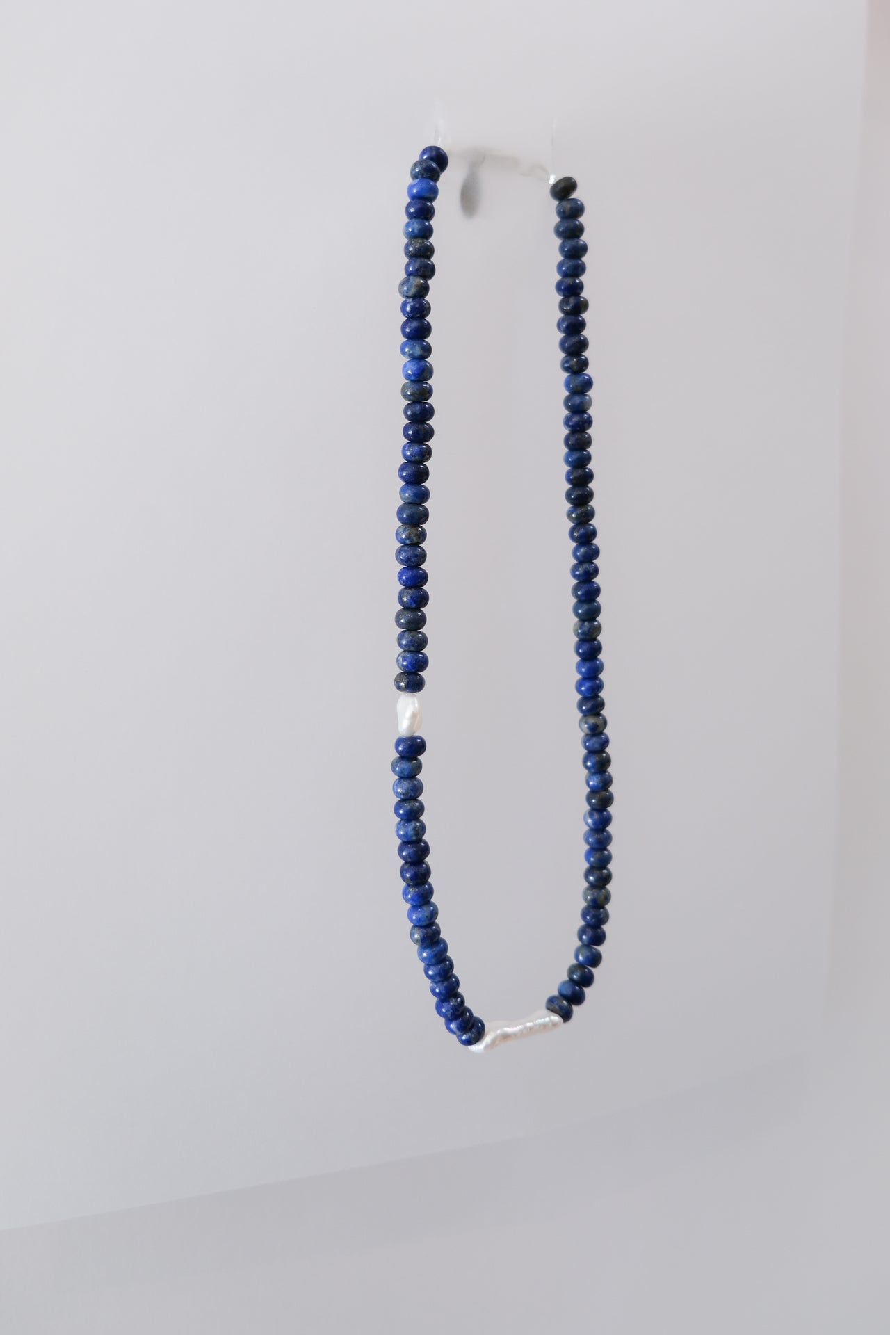 A lapis lazuli beaded necklace with a silver clasp and fresh water pearls, displayed against a white background.