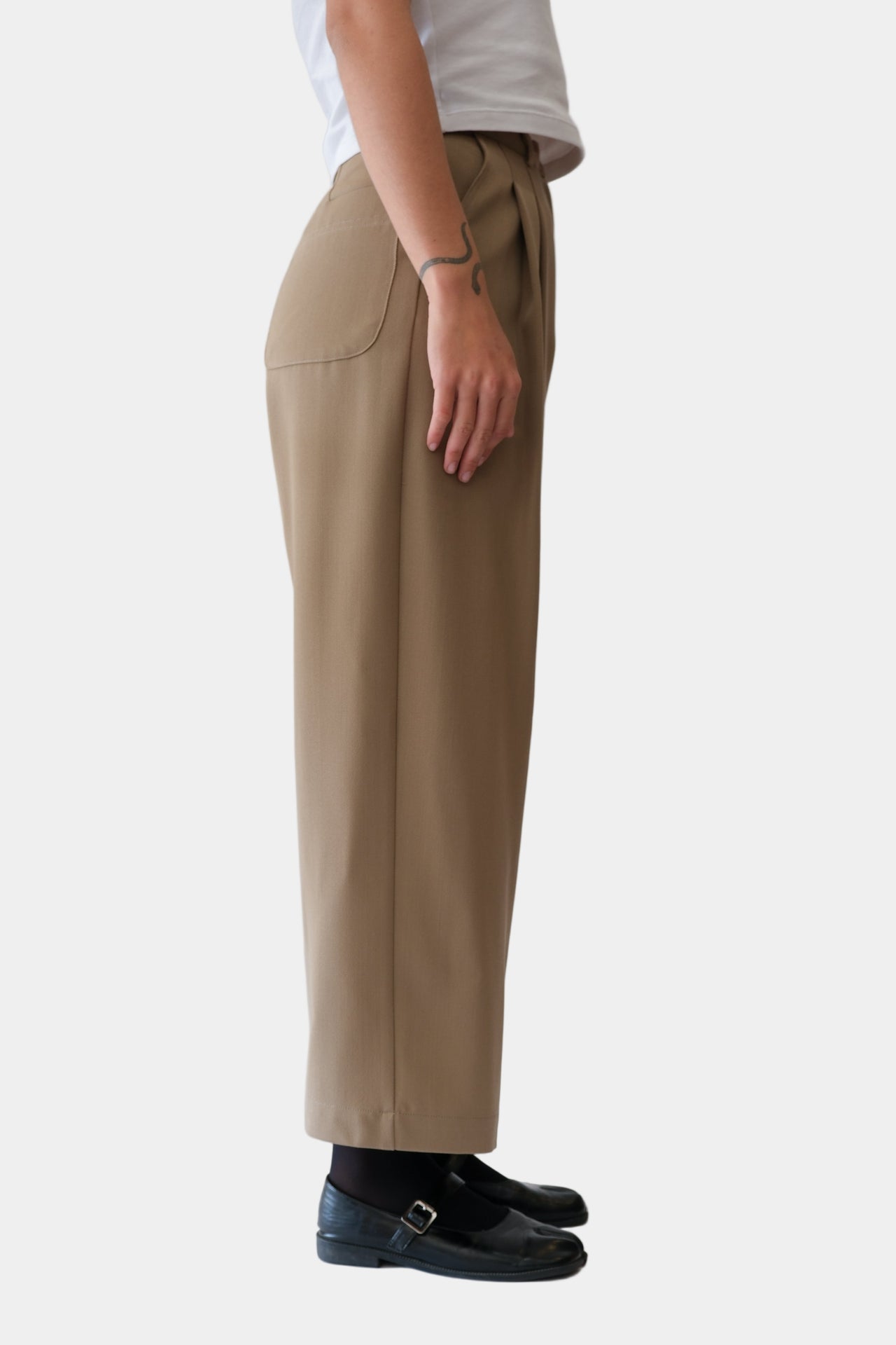A pair of beige wool trousers with double front pleats, side entry pockets, and a hook and bar fastening. The trousers are displayed on a model against a white background.