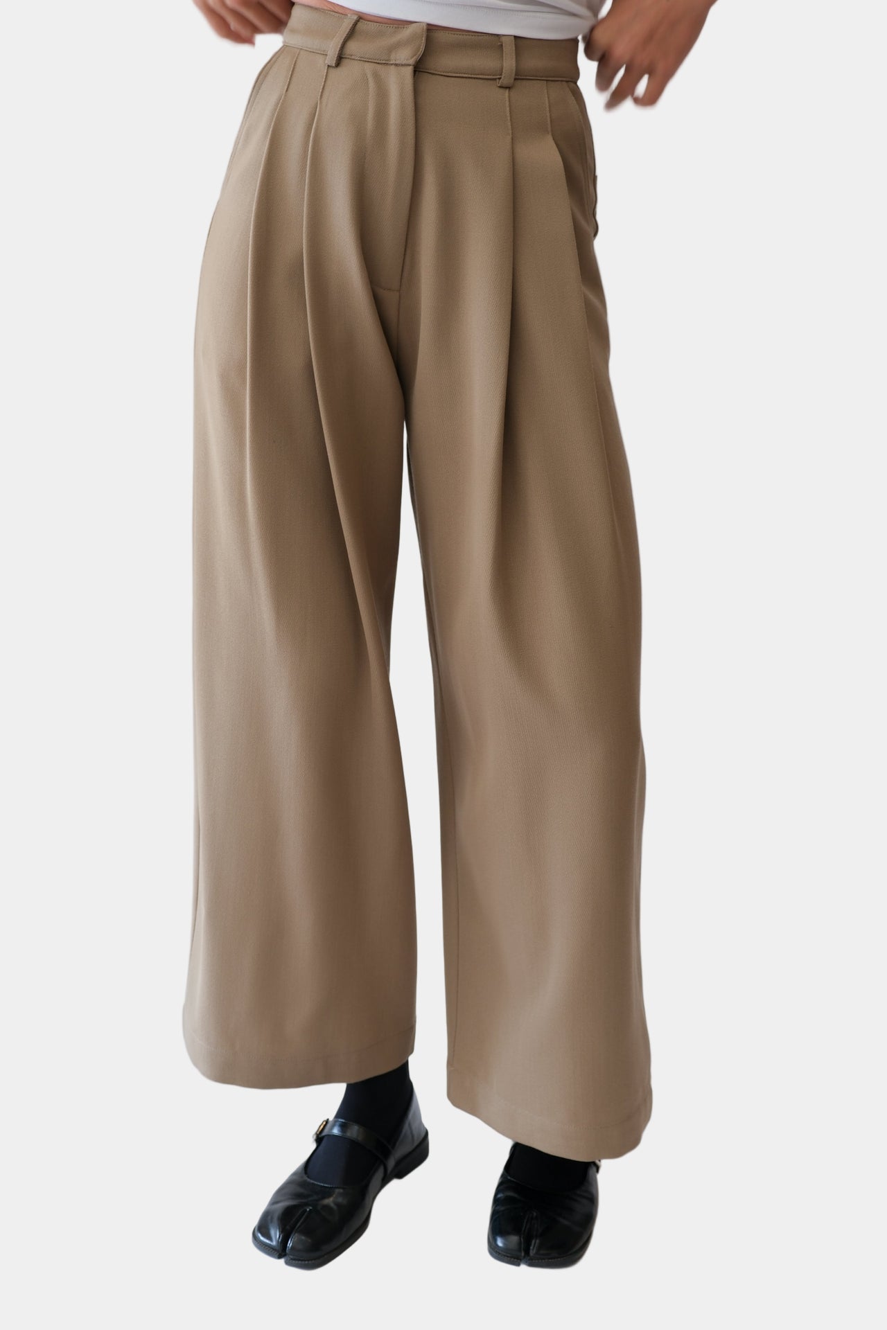 A pair of beige wool trousers with double front pleats, side entry pockets, and a hook and bar fastening. The trousers are displayed on a model against a white background.