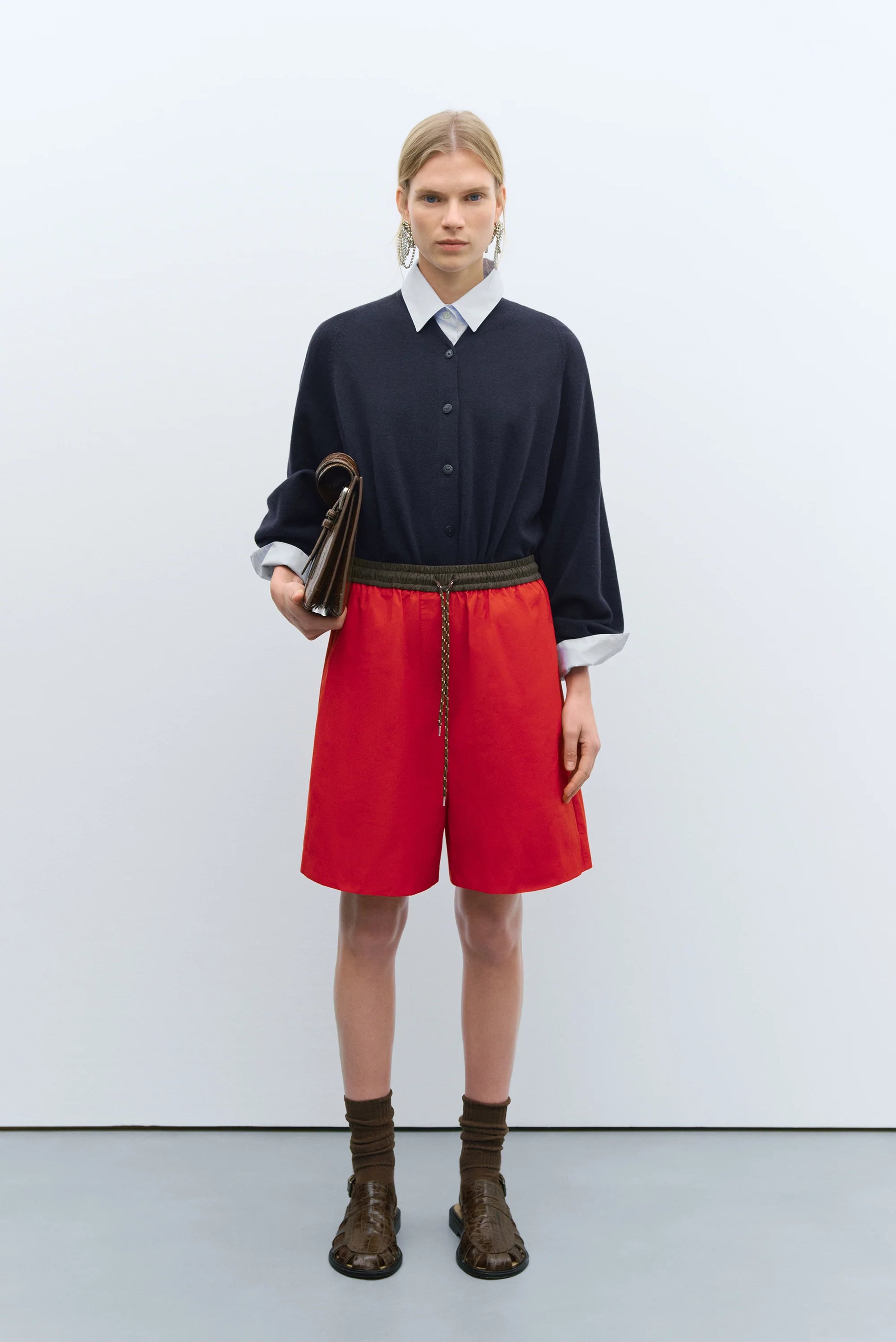Person wearing a navy sweater, white shirt, red shorts, and brown boots on a white background