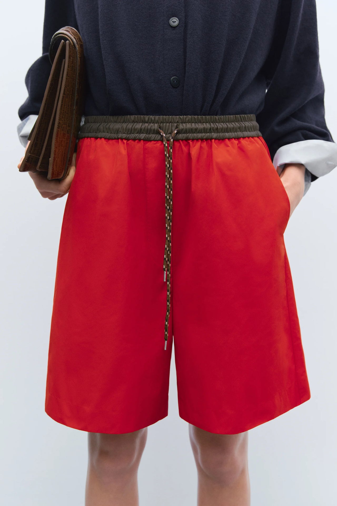 Person wearing a red skirt with a black top and brown bag on a white background