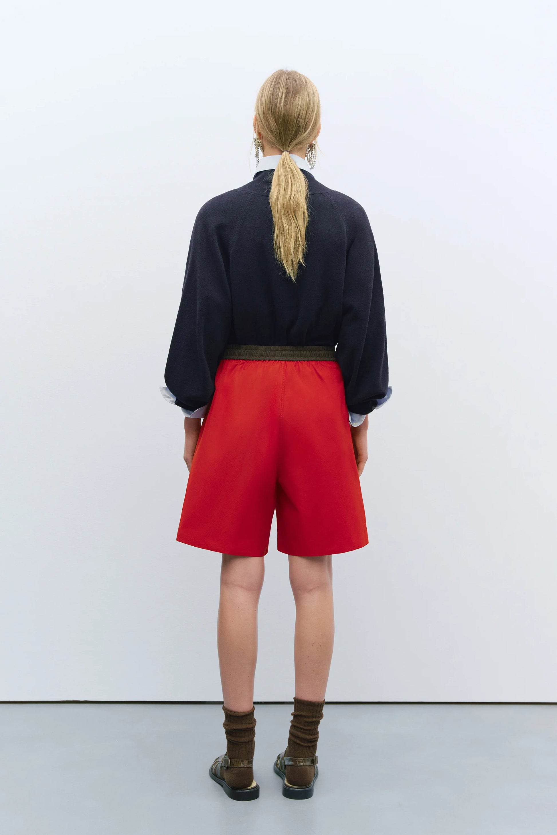 Person wearing a black top and red shorts standing against a white wall.