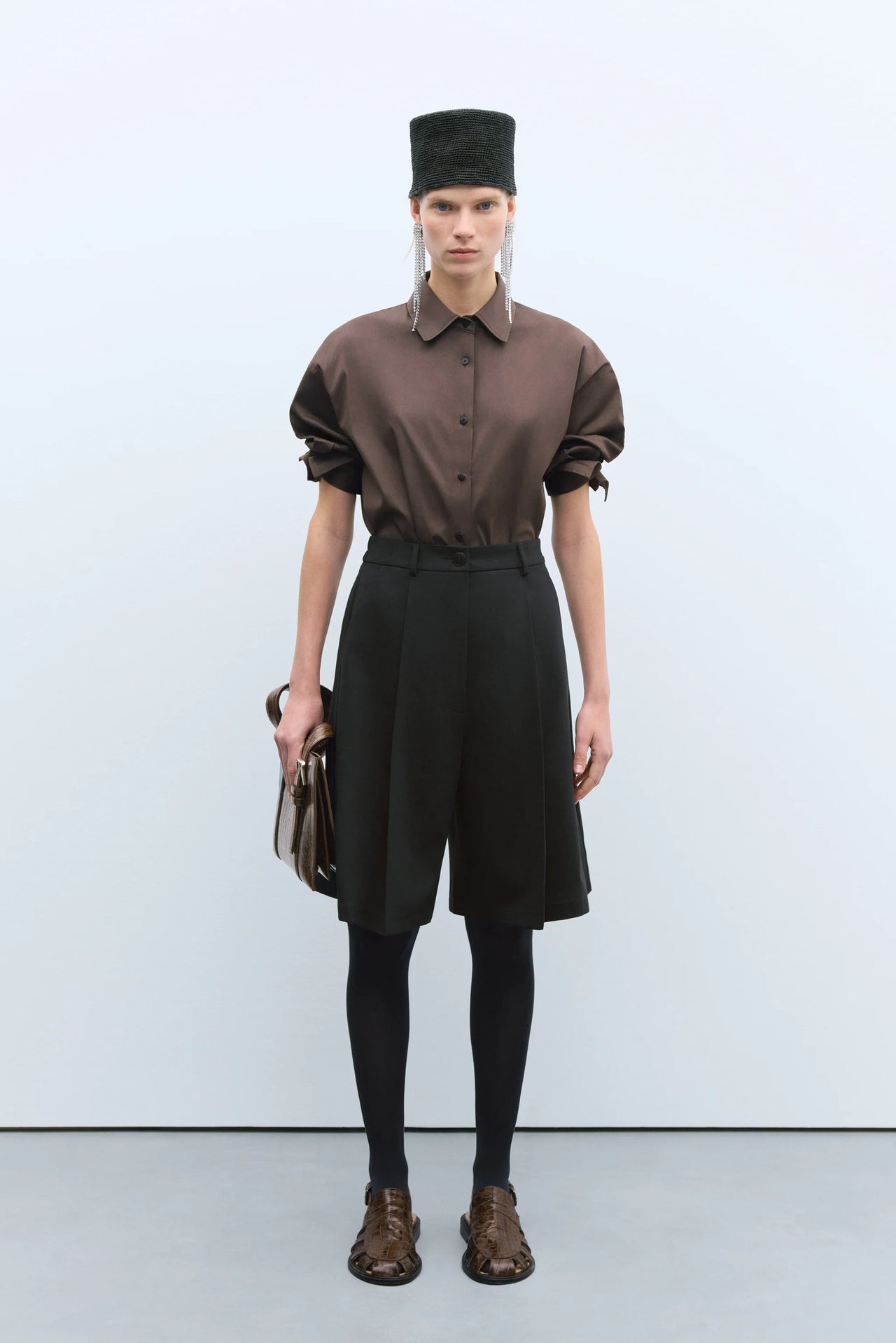 Person wearing a brown shirt, black skirt, and hat against a white background