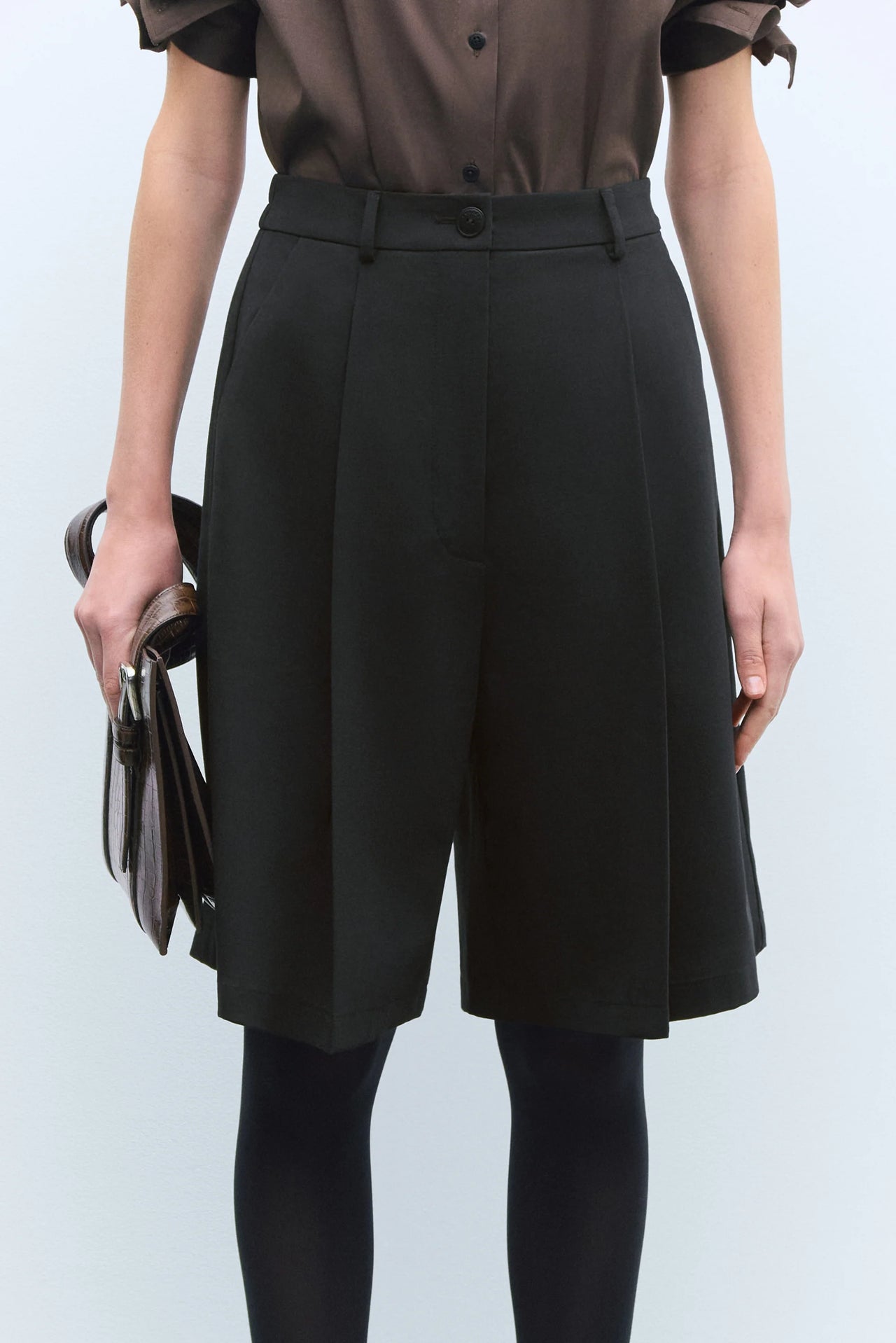 Person wearing a brown shirt, black skirt, and hat against a white background