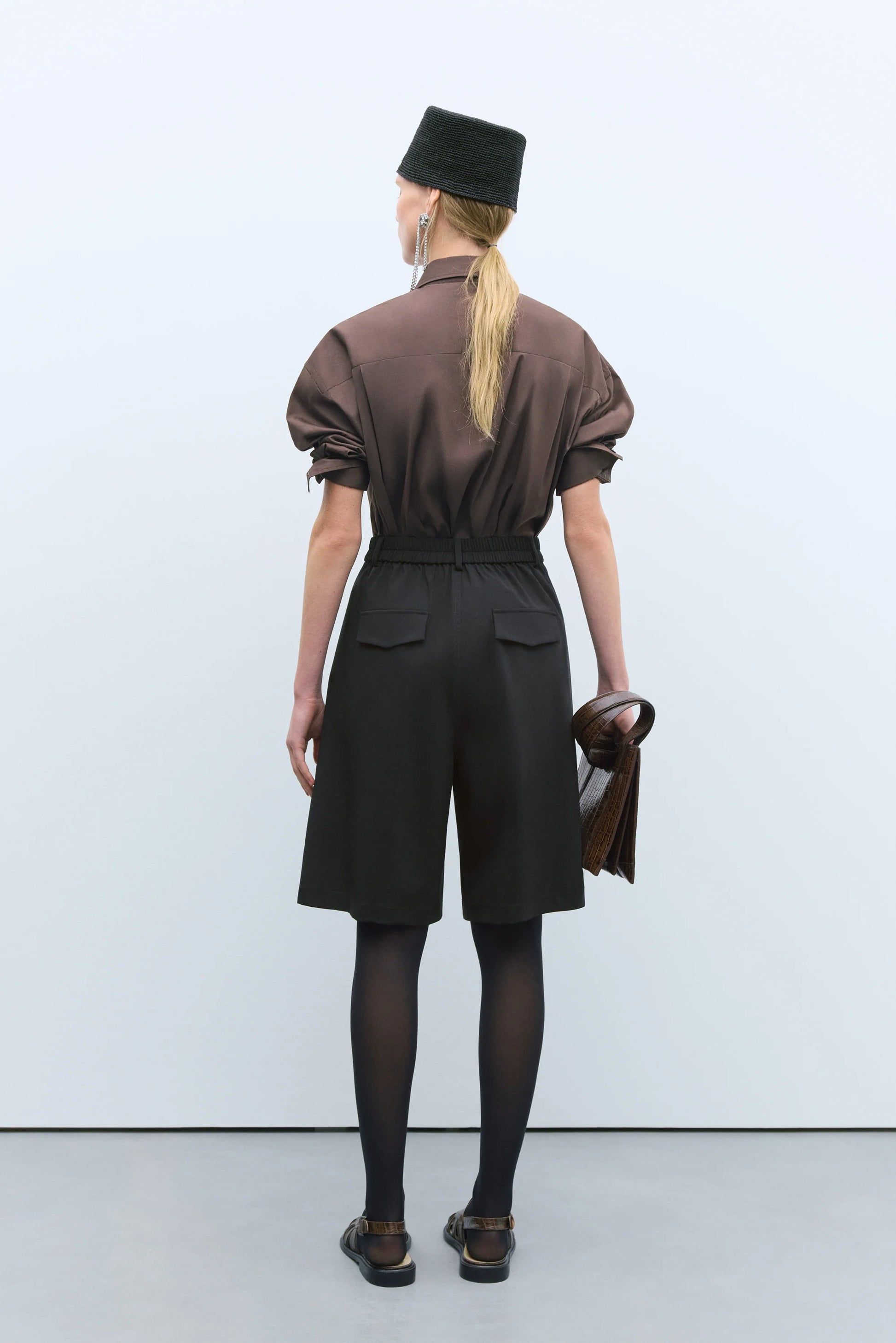Person wearing a brown shirt and black shorts with a black hat against a white background