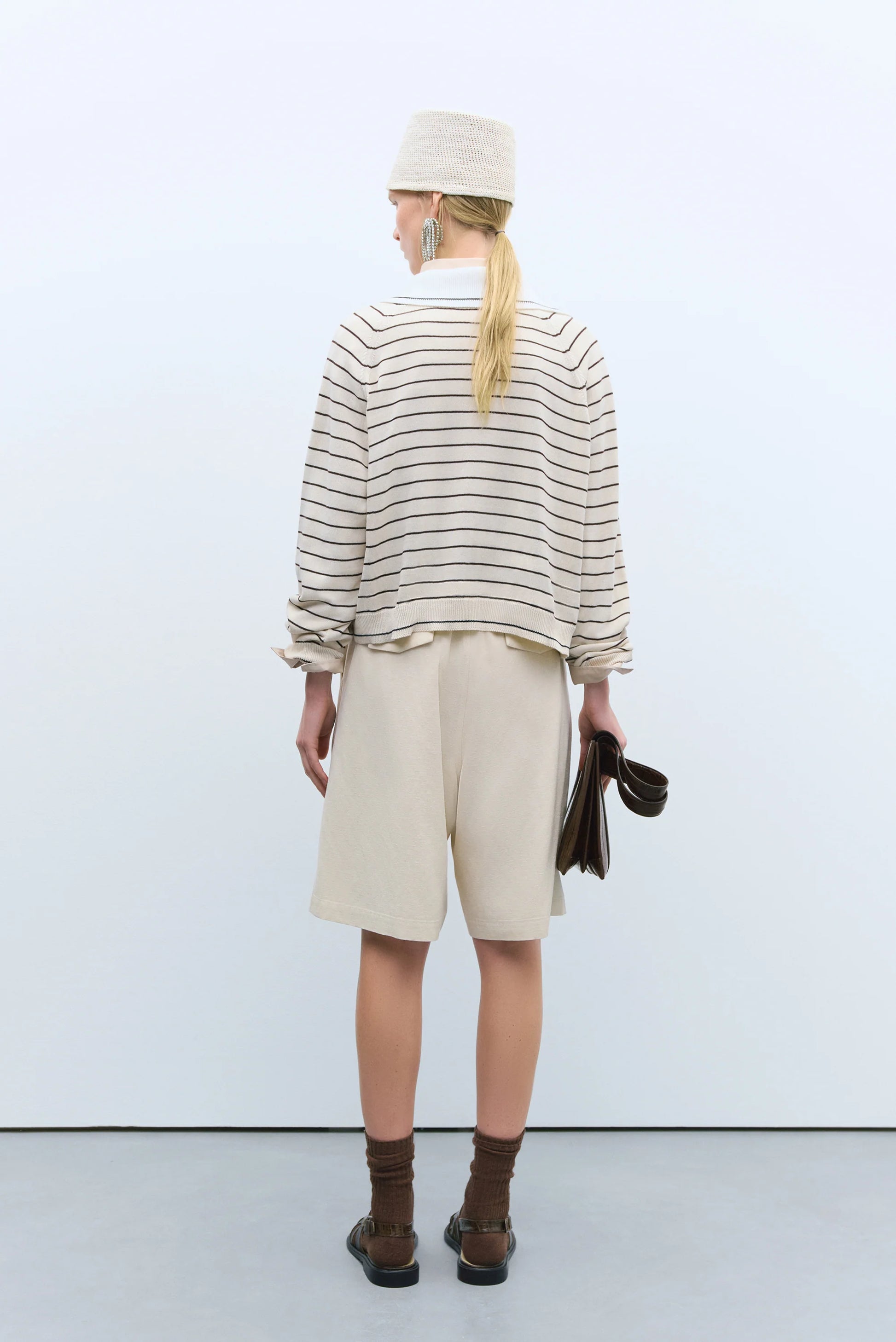 Person wearing a striped shirt, beige shorts, and brown shoes against a white background