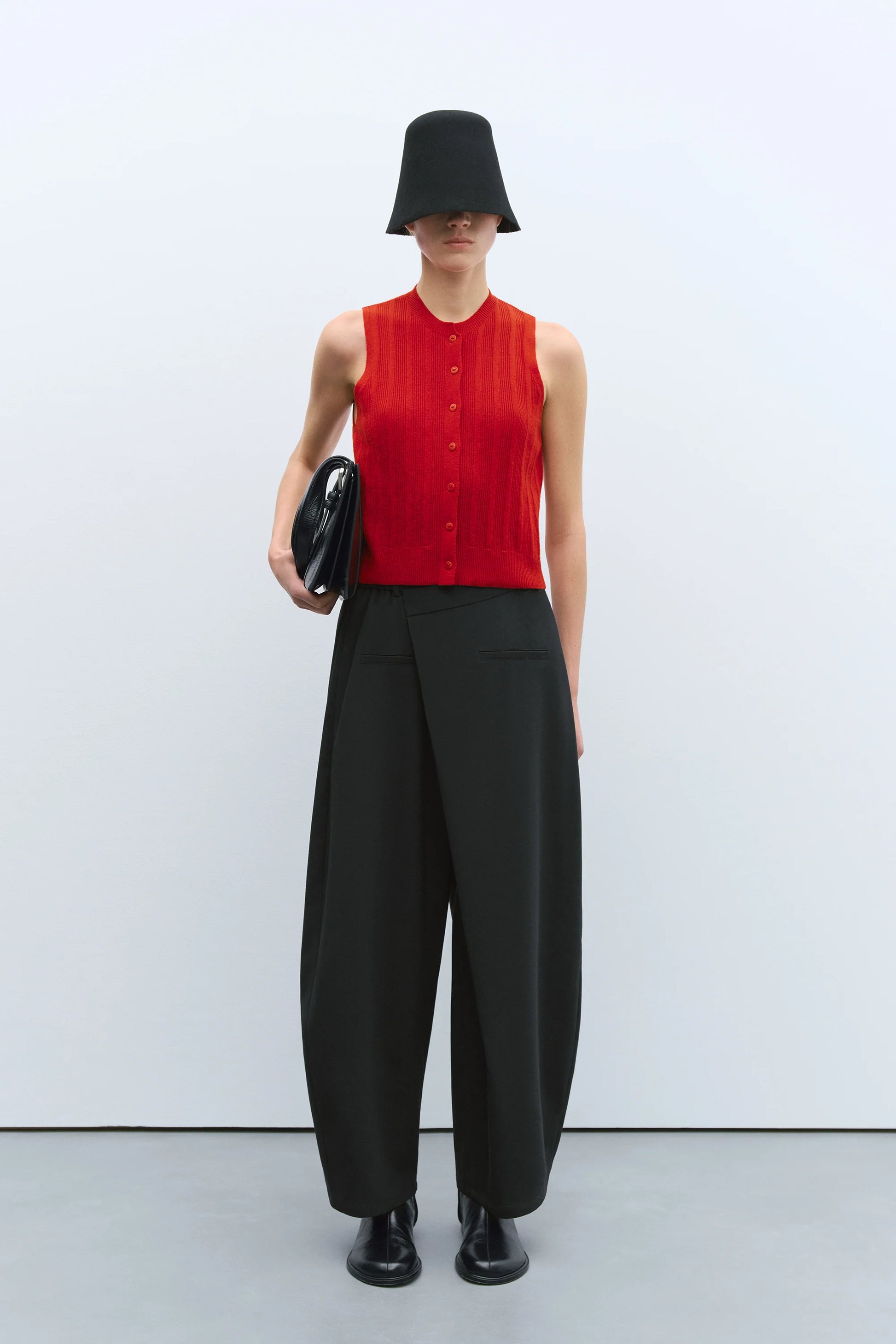 Person wearing a red sleeveless top and black wide-leg pants with a black hat on a white background
