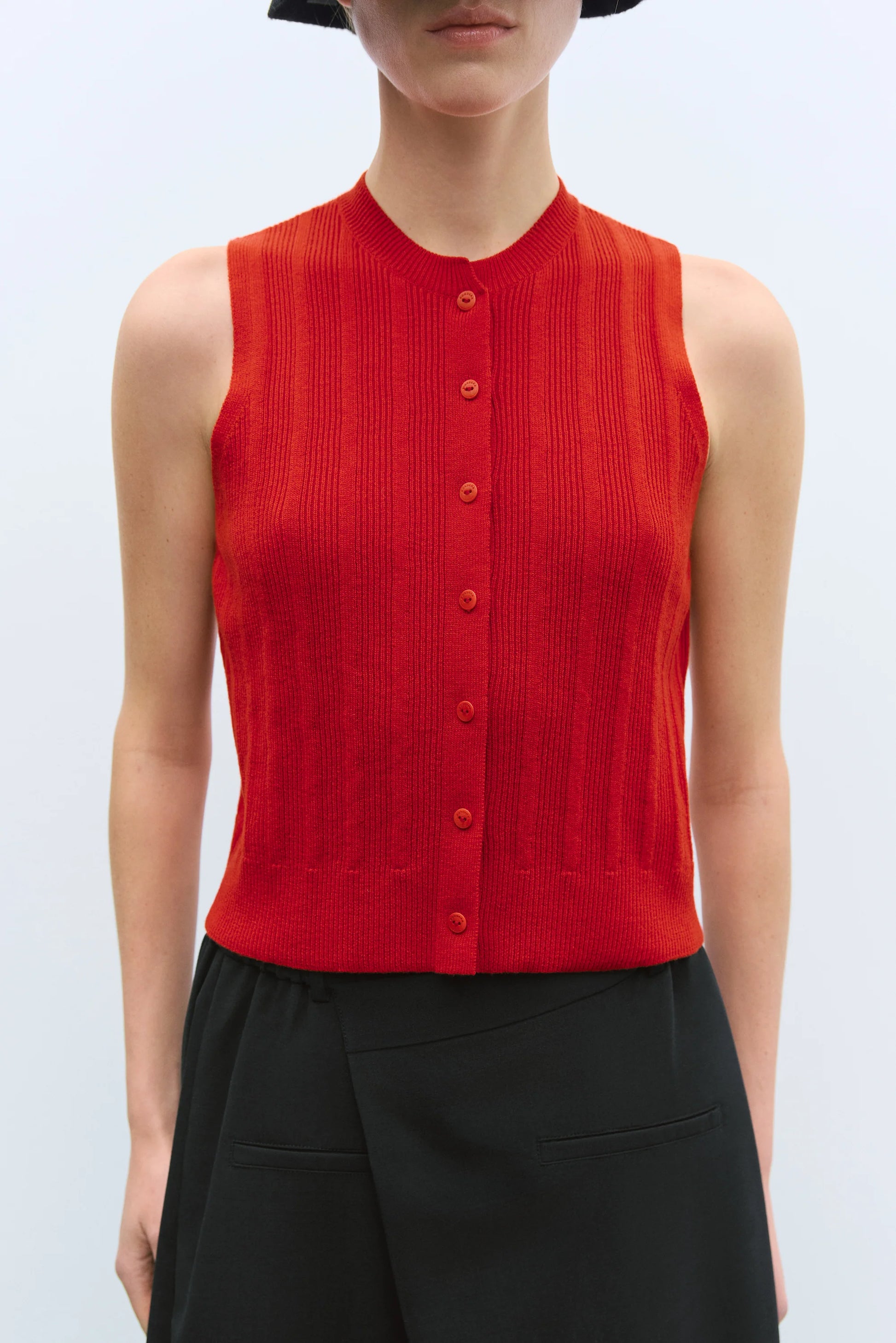 Person wearing a red sleeveless button-up top against a light blue background