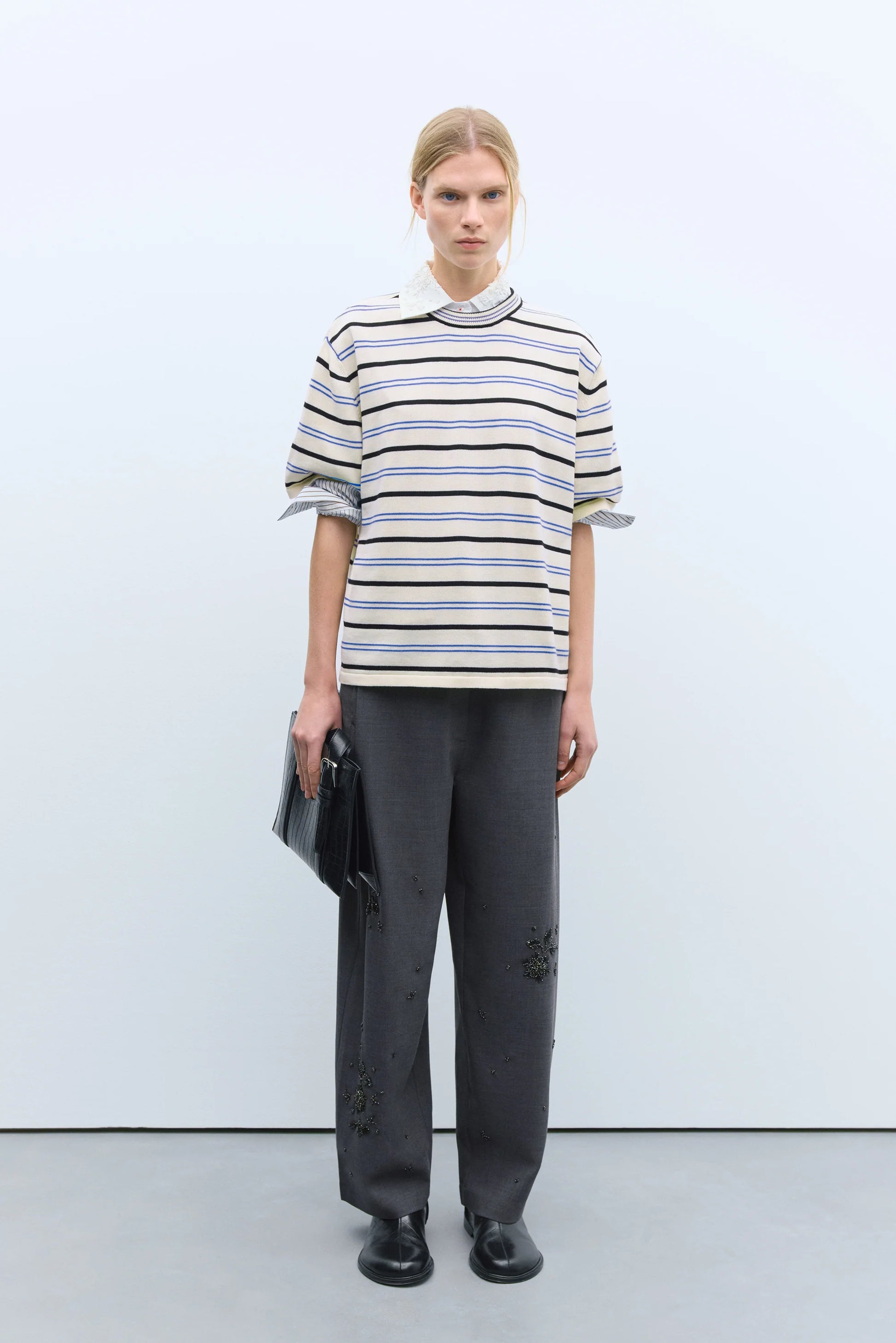 Person wearing a striped shirt and black pants against a white background