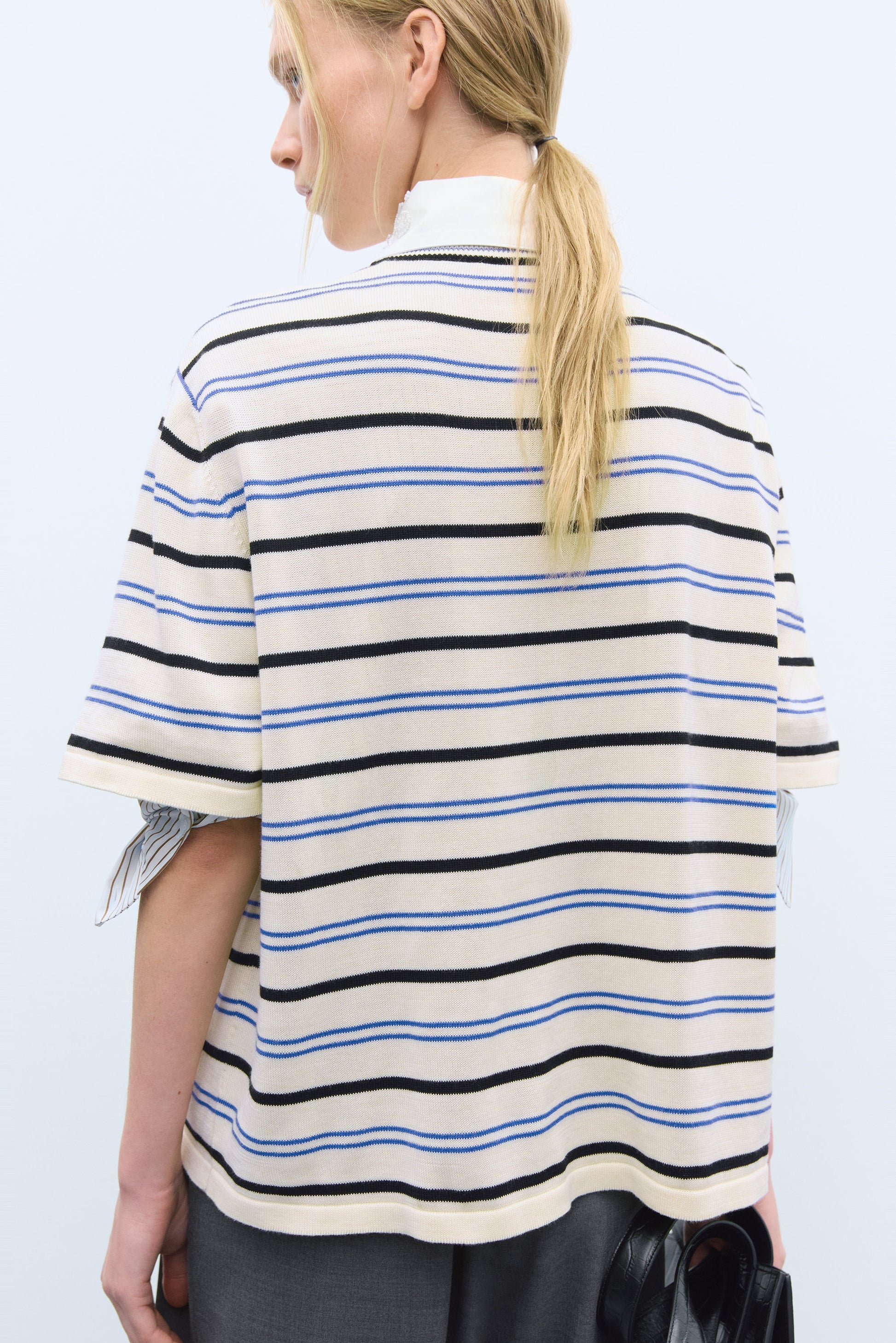 Woman wearing a striped shirt with black, blue, and white horizontal lines on a plain background