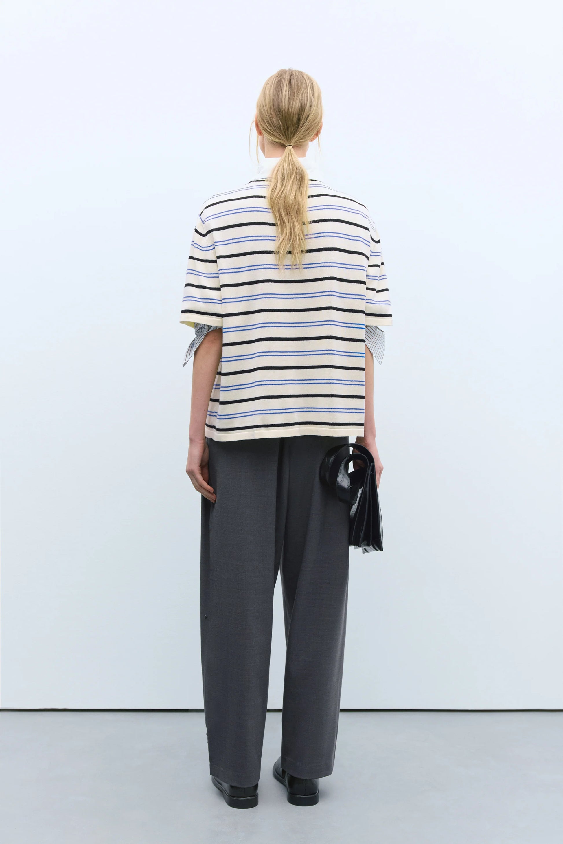 Person wearing a striped shirt and gray pants against a white background