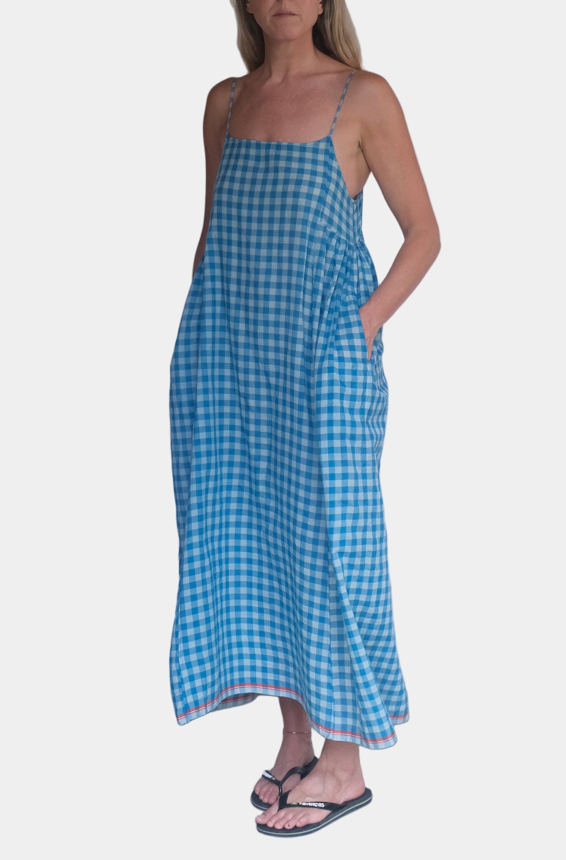 Woman wearing a blue checkered dress standing against a white wall.