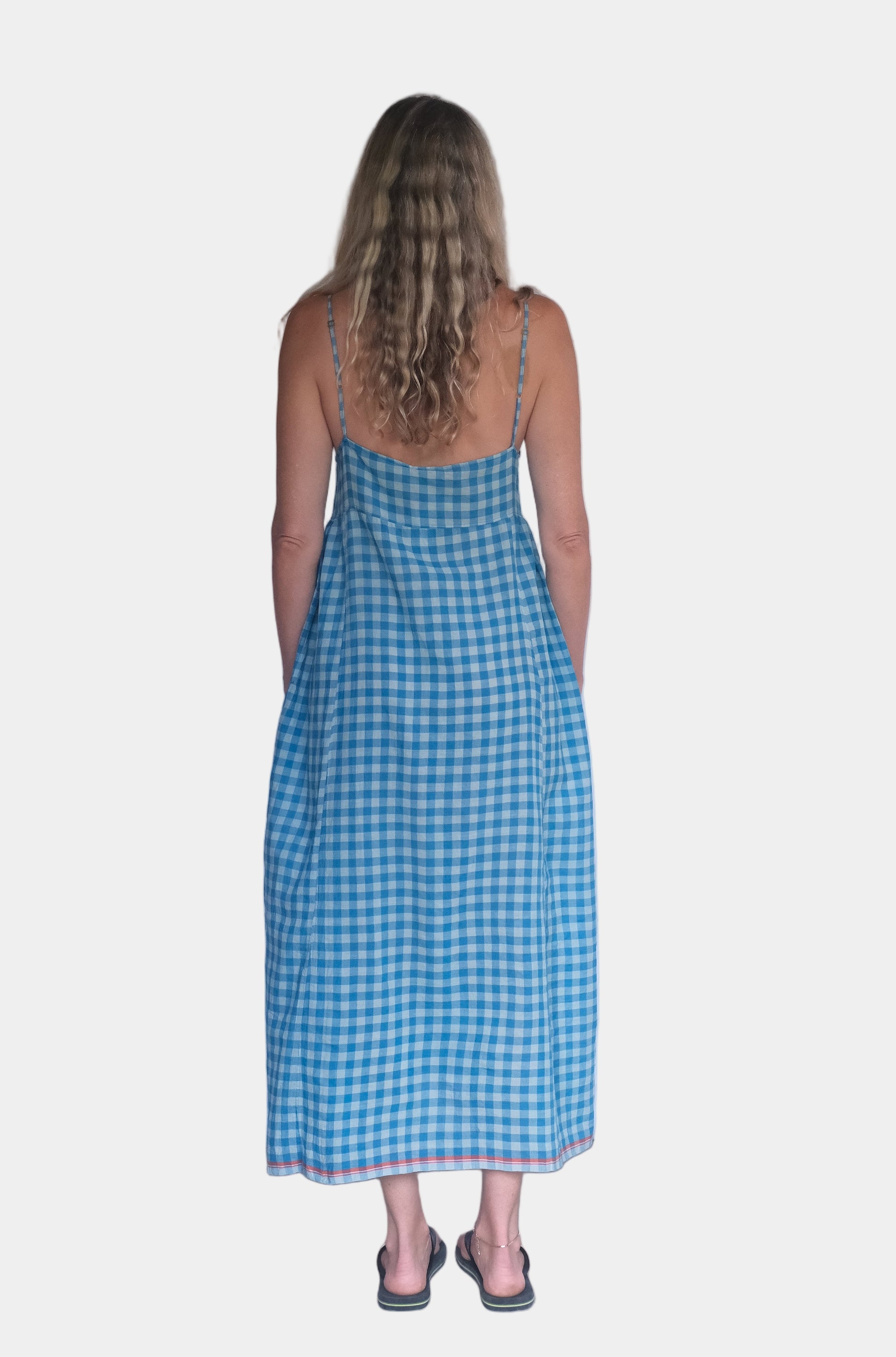 Woman wearing a blue checkered dress standing in front of a white background.