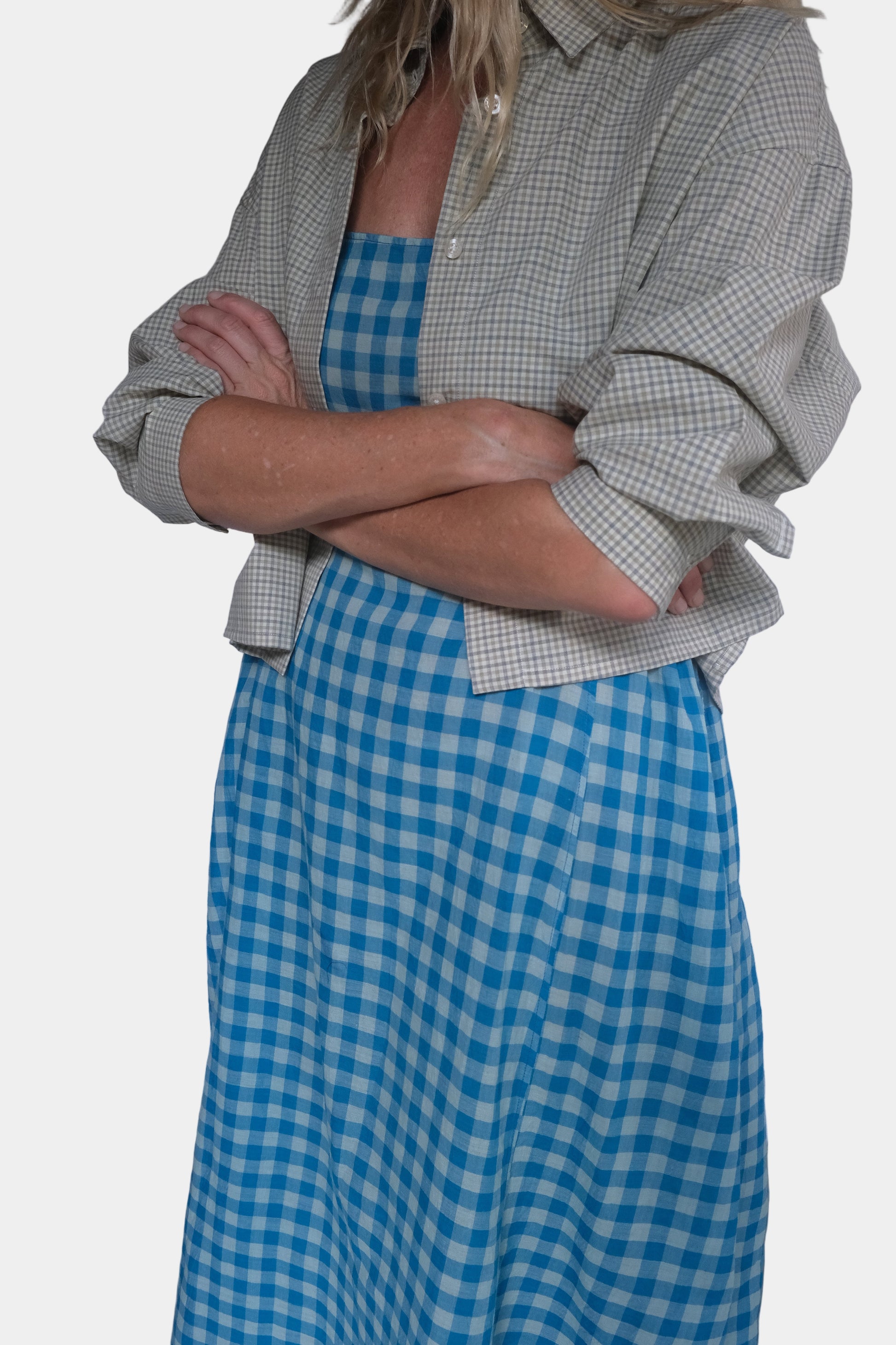 Person wearing a green checkered shirt and blue gingham skirt against a white background