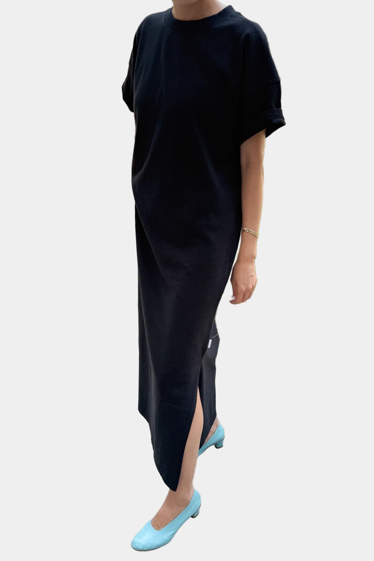 Person wearing a black dress with a slit and light blue shoes ahainst a white background.