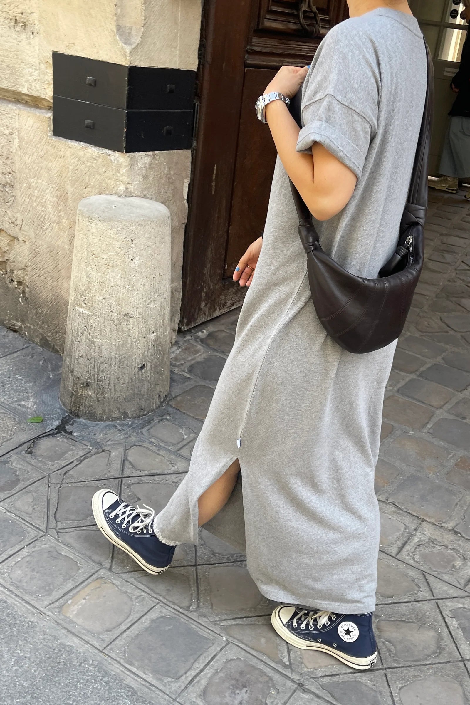 Person wearing a long gray dress and blue sneakers on a street.