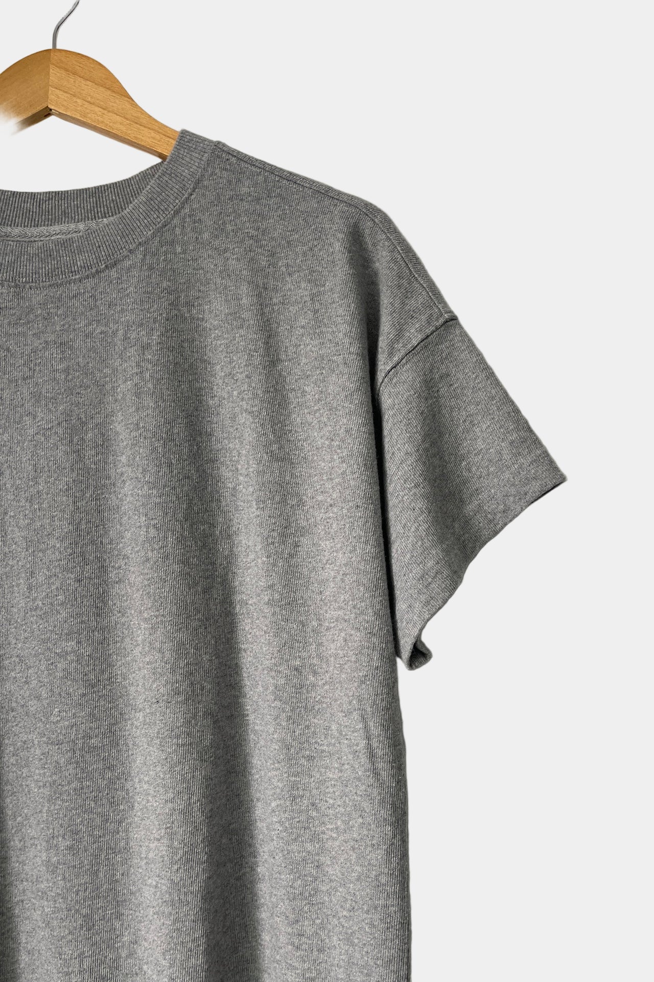 Gray t-shirt on a wooden hanger against a white wall