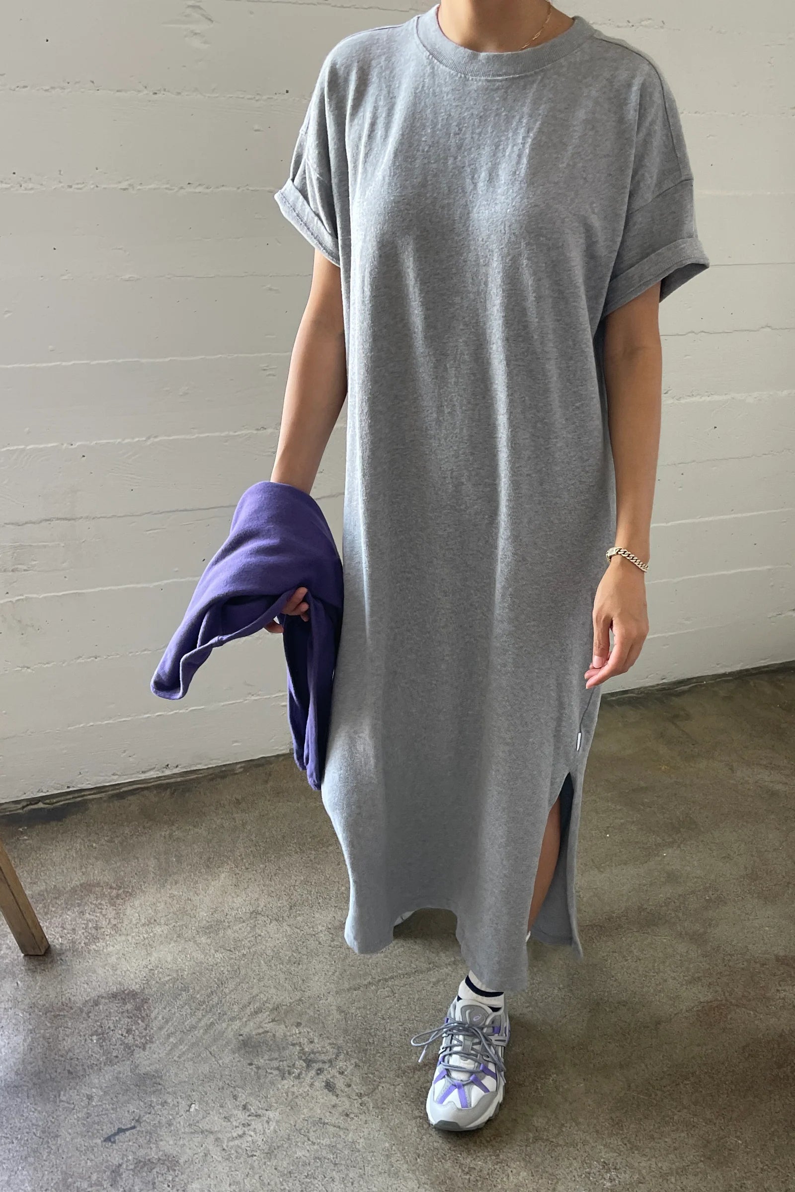 Person wearing a long gray t-shirt with a white wall background
