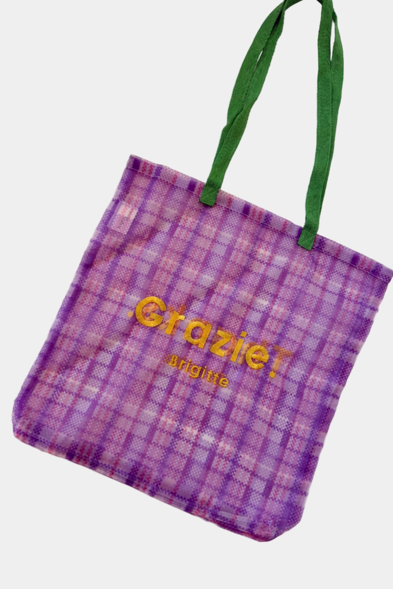 Purple checkered tote bag with green handles on a light pink background