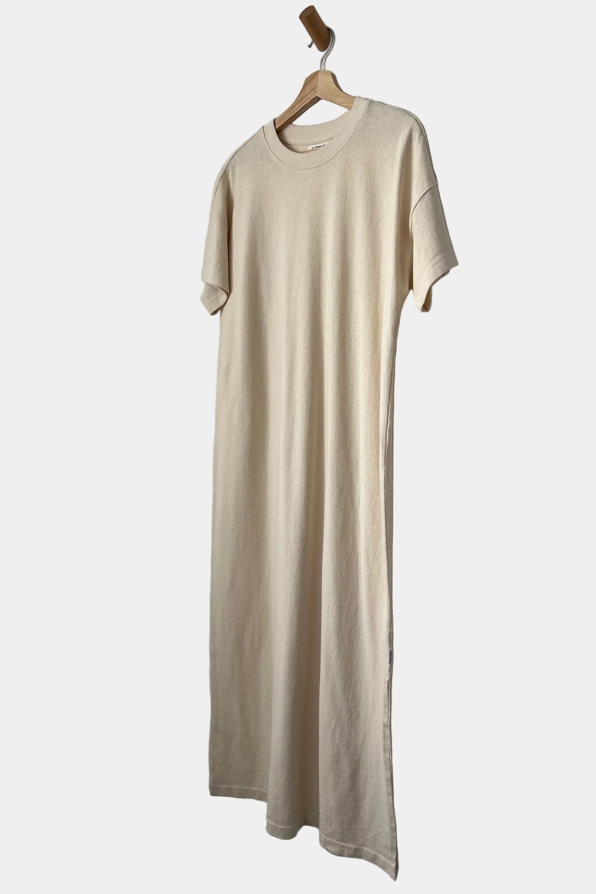 Beige dress hanging on a wooden hanger against a white wall