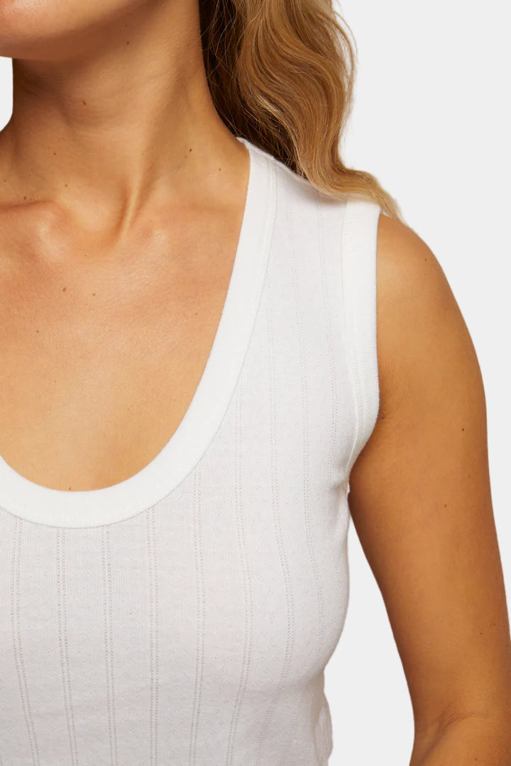 Close-up of a person wearing a white tank top against a neutral background
