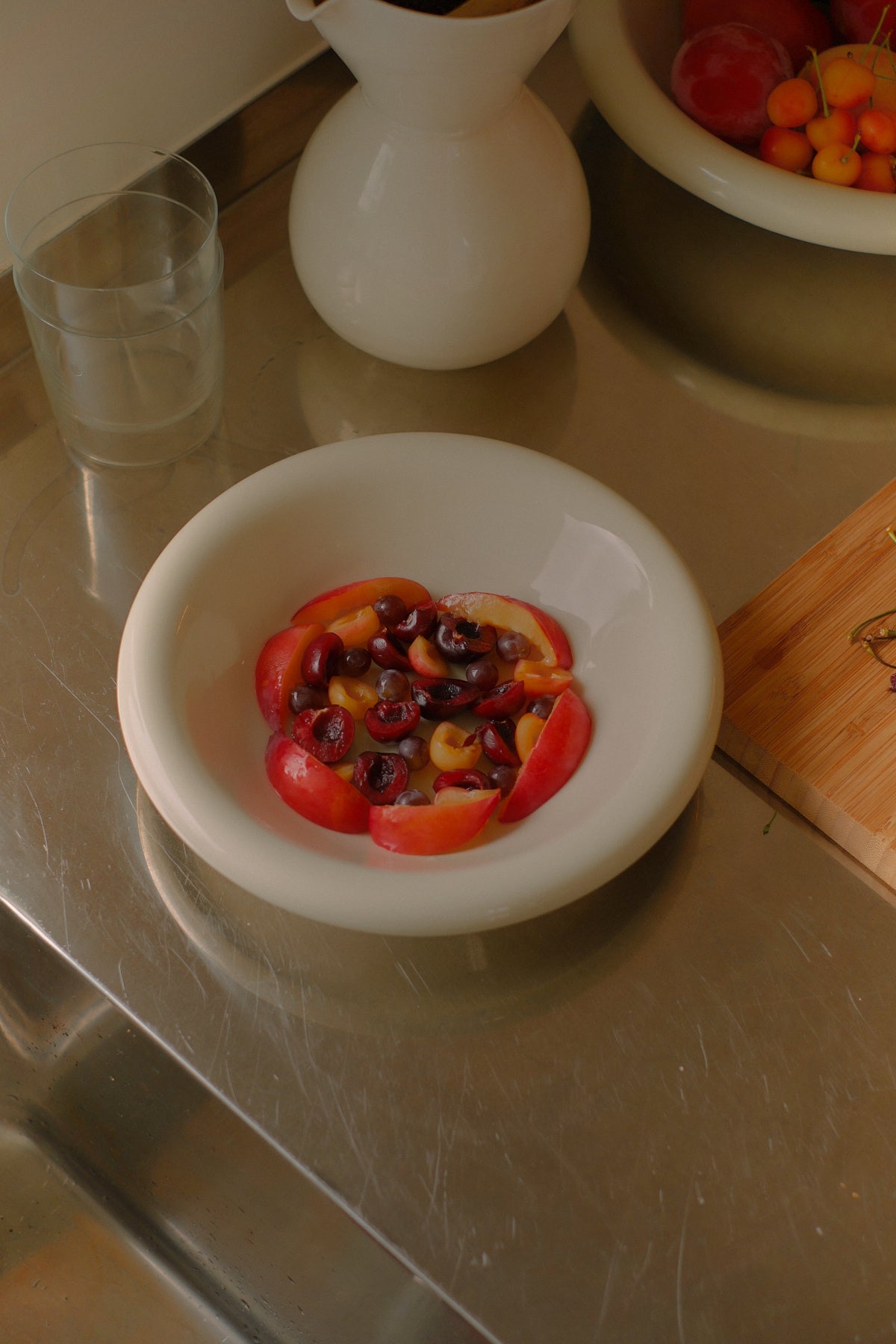 Everything Bowl in Marshmallow filled with fruit, on a stainless steel surface with other ceramics and glass ware