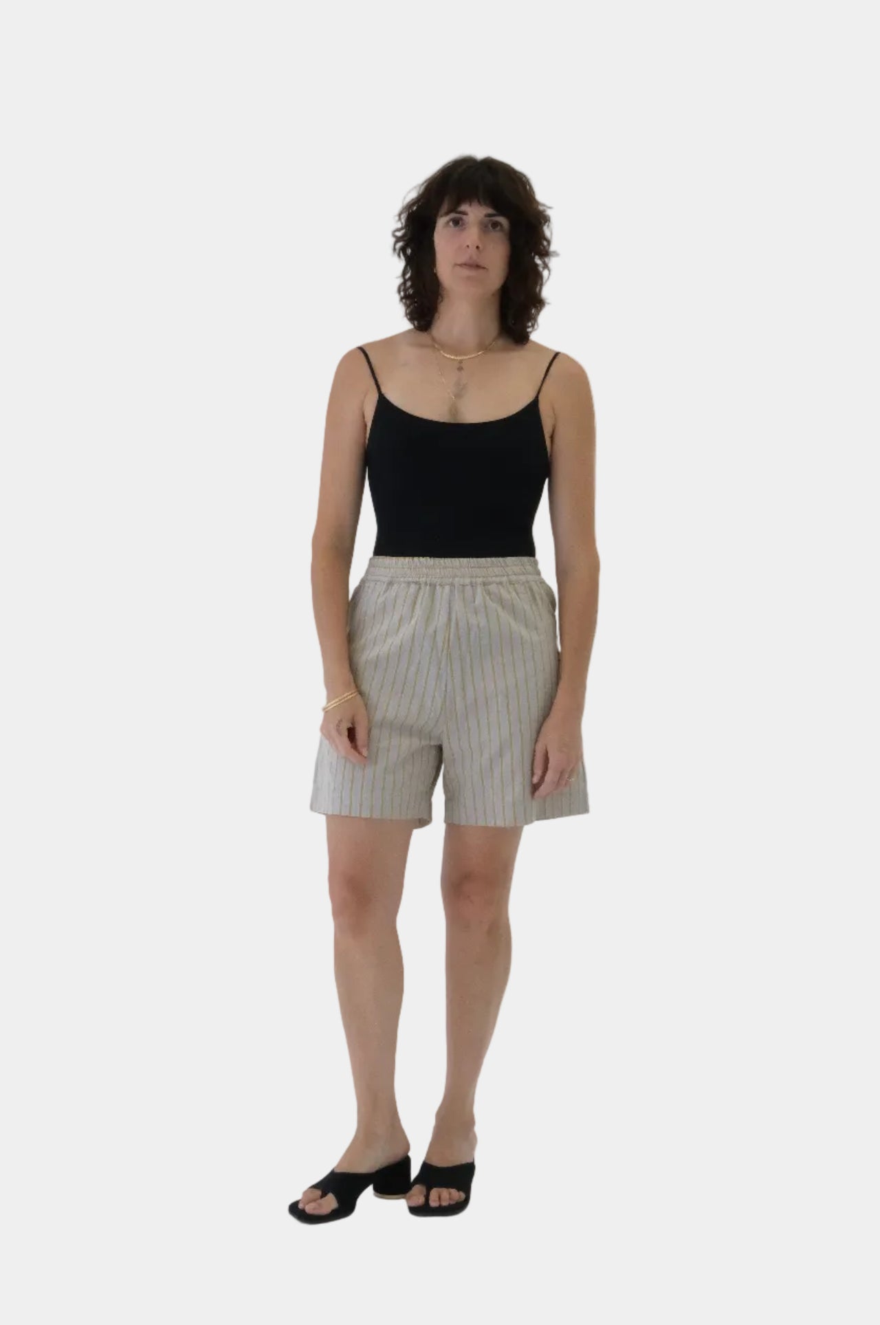 Woman wearing a black tank top and beige shorts on a white background