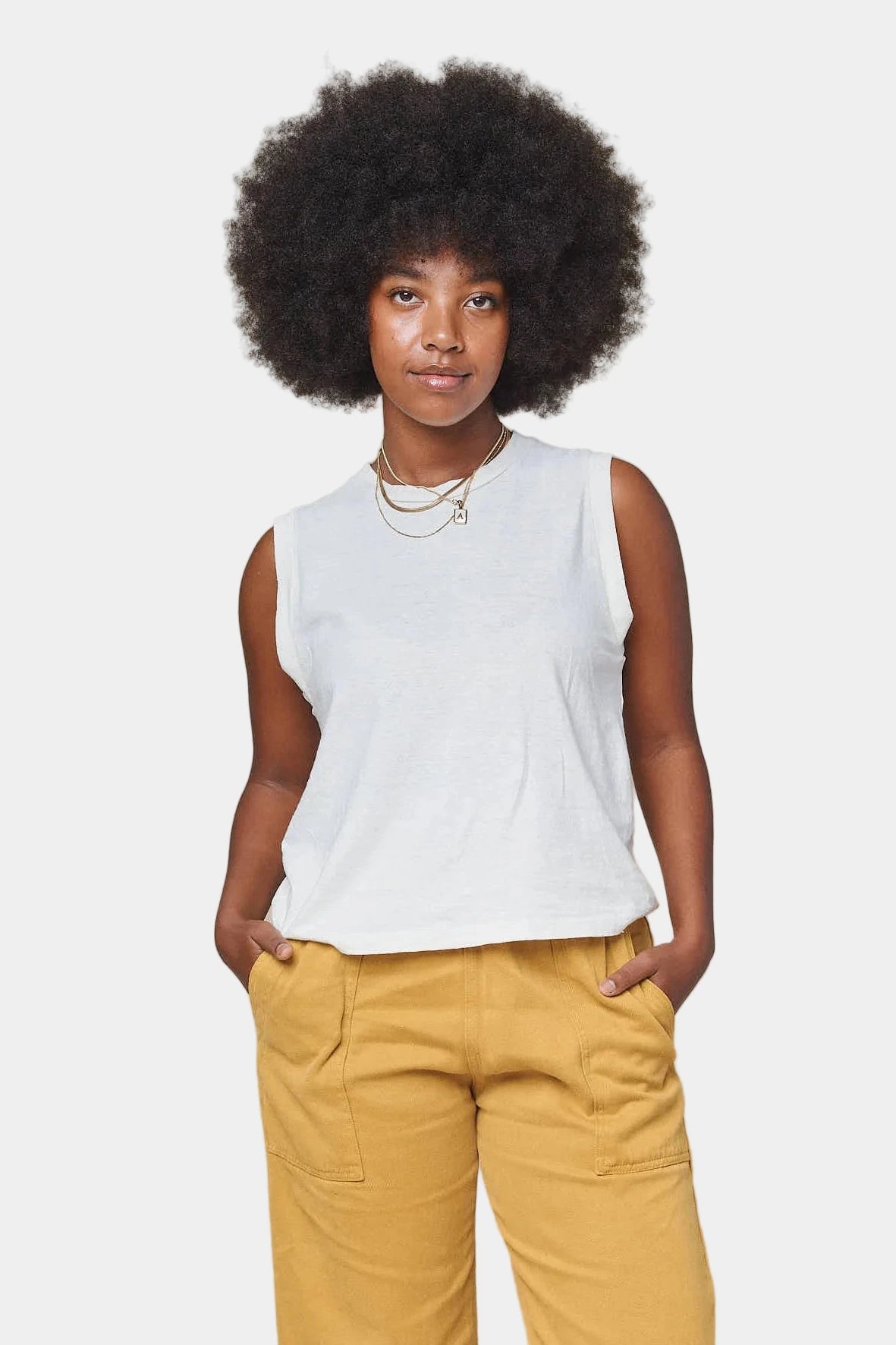 Woman wearing a white sleeveless top and yellow pants against a white background
