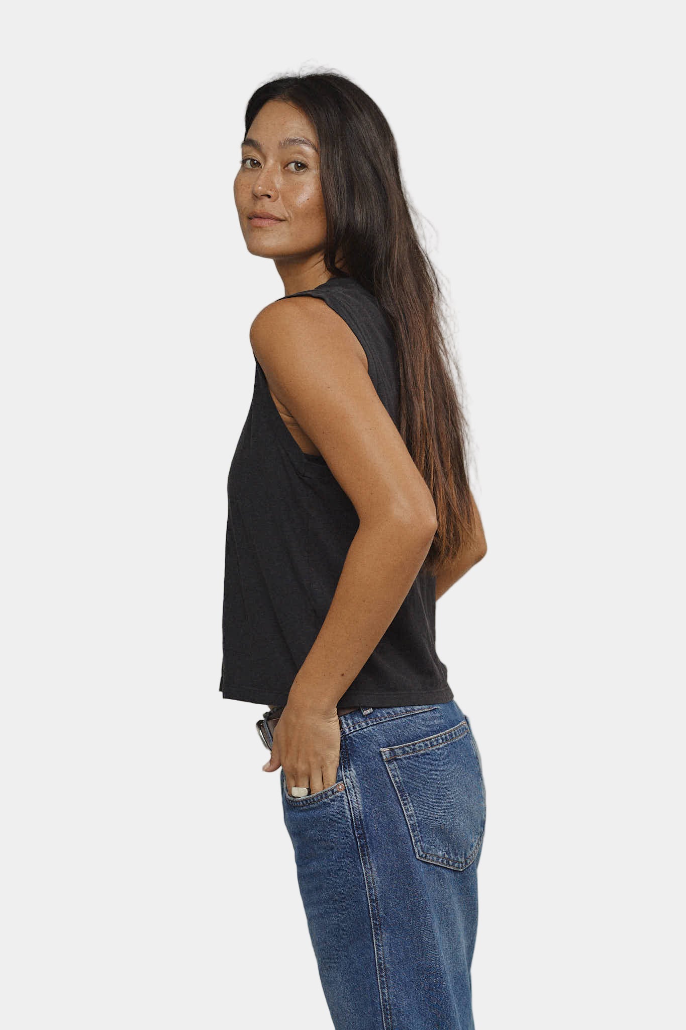 Woman wearing a black sleeveless top and blue jeans against a plain background