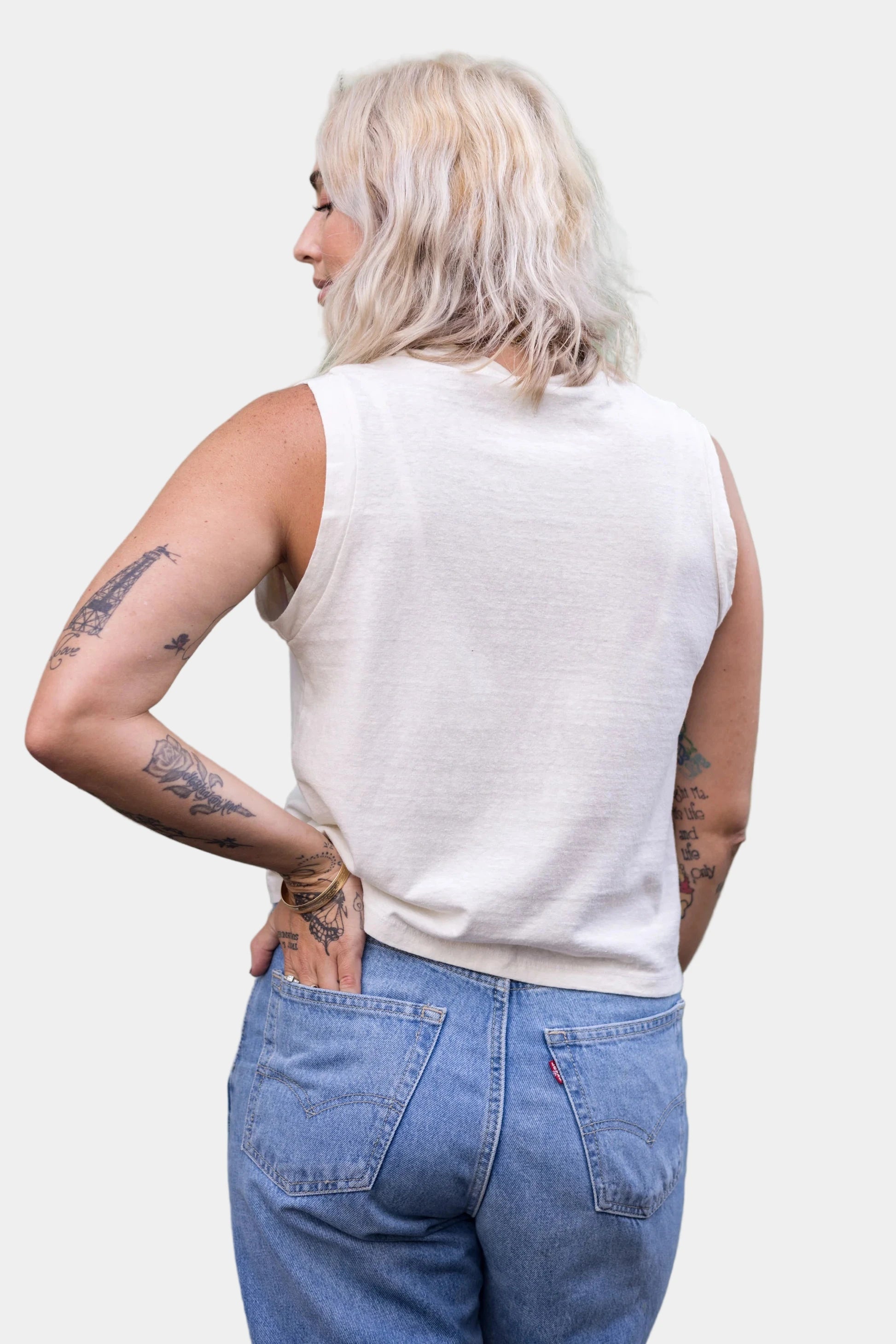 Person wearing a white sleeveless top and blue jeans against a plain background