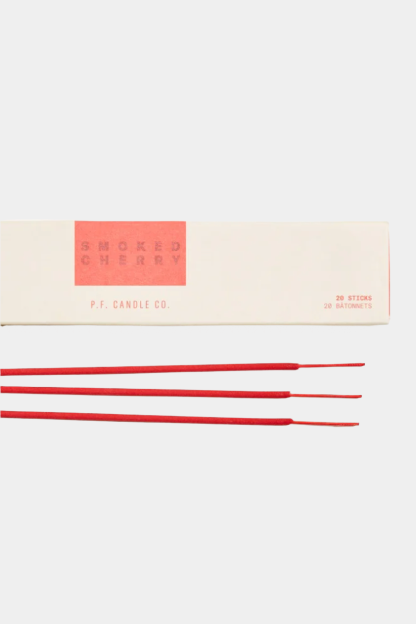 A pack of incense sticks with red coloring on them, placed in front of their packaging which has a minimalist design.