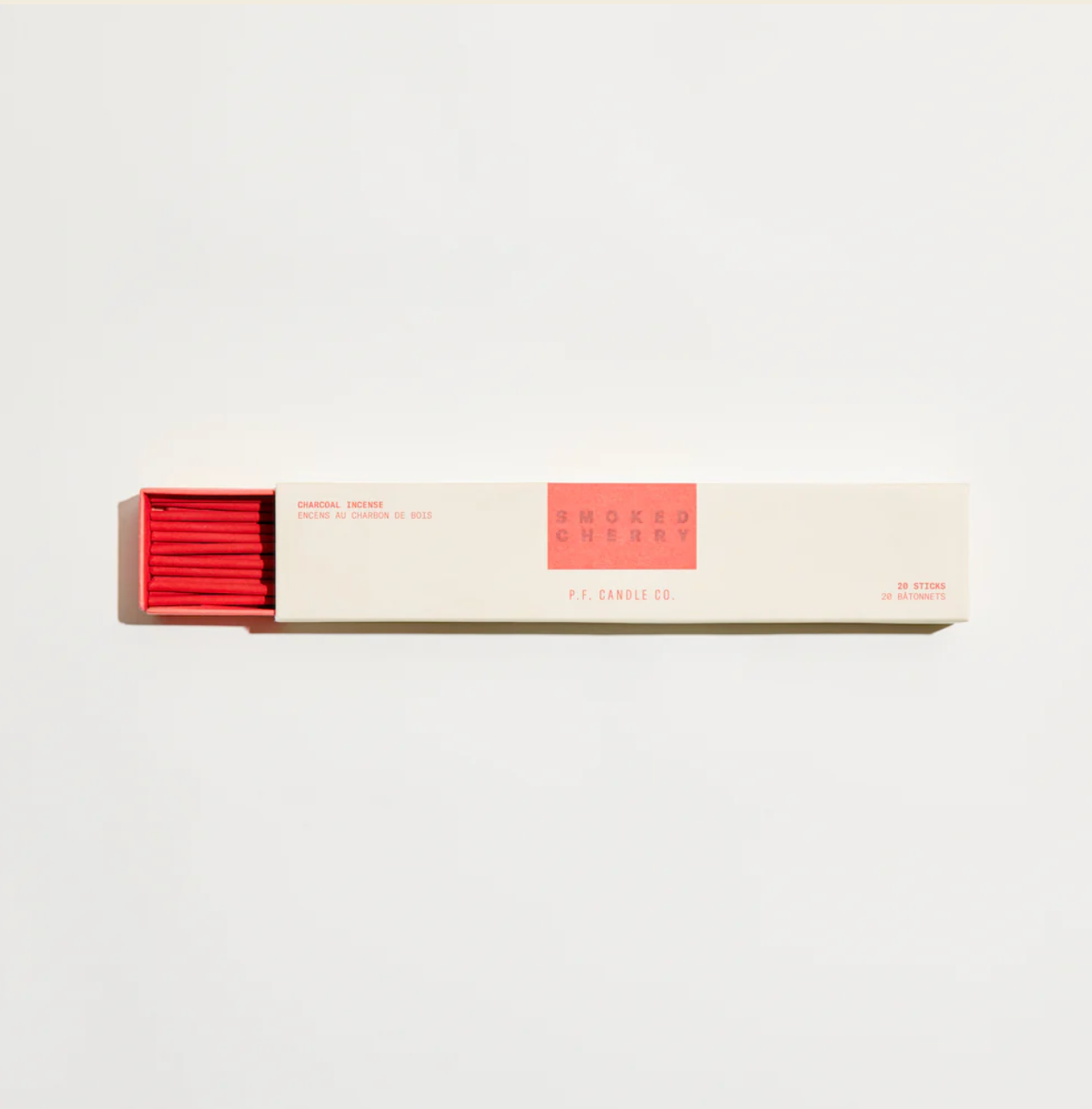 A pack of incense sticks with red coloring on them, placed in front of their packaging which has a minimalist design.