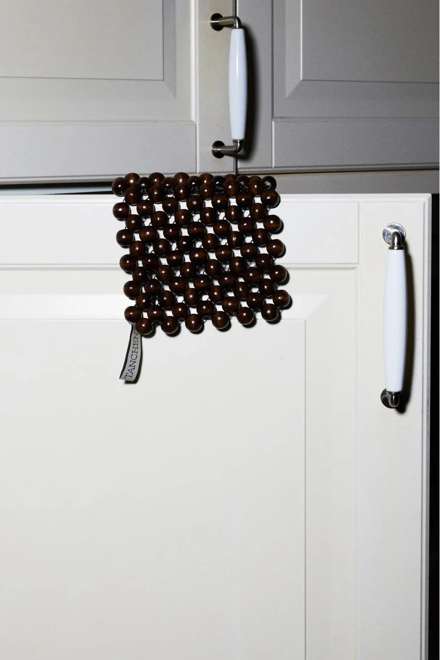 Brown beaded mat with a brand label on a light gray background