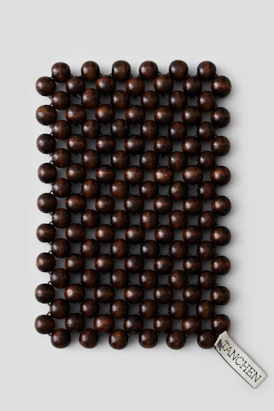 Brown beaded mat with a brand label on a light gray background