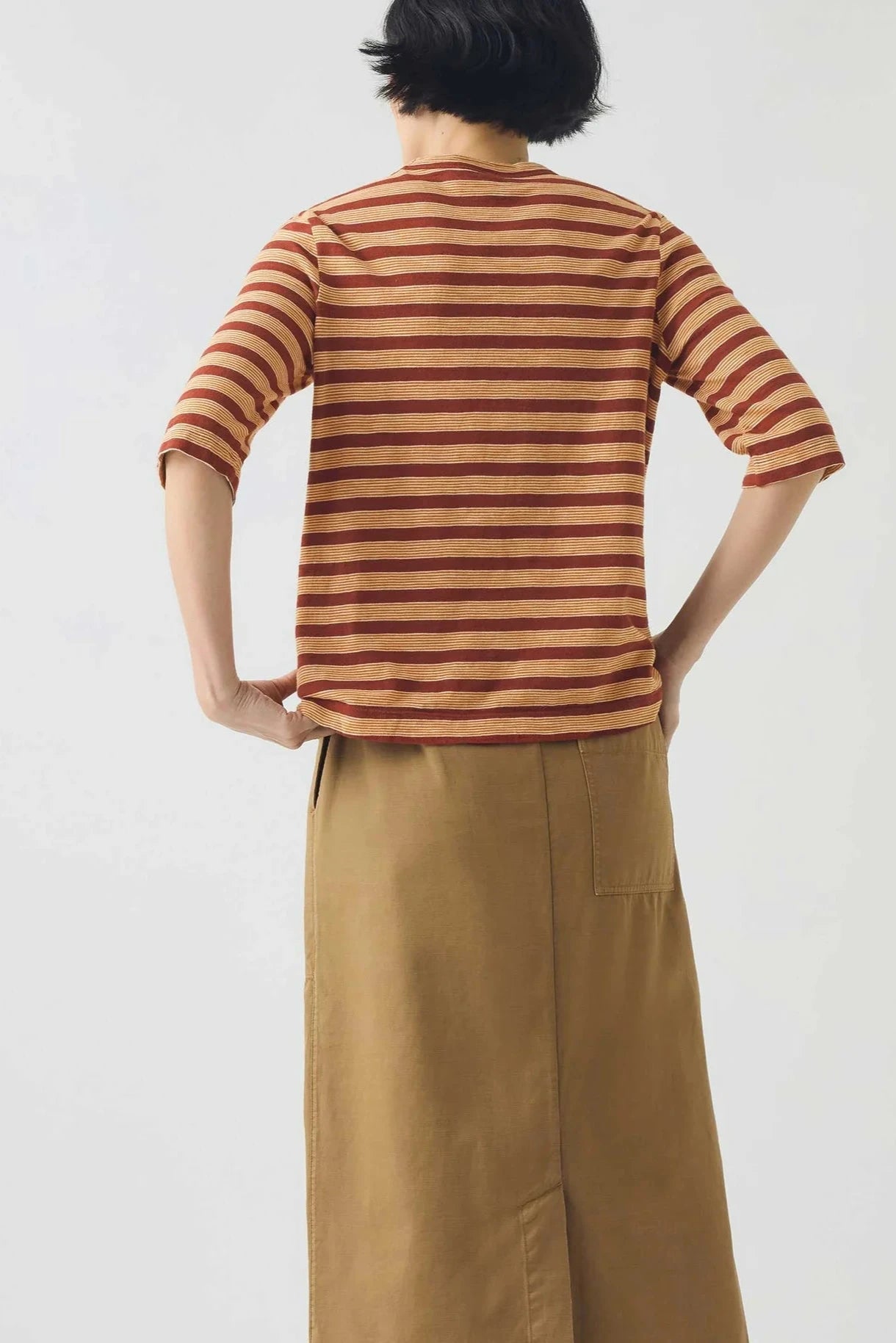 Person wearing a striped shirt and beige pants against a white background, viewed from the back